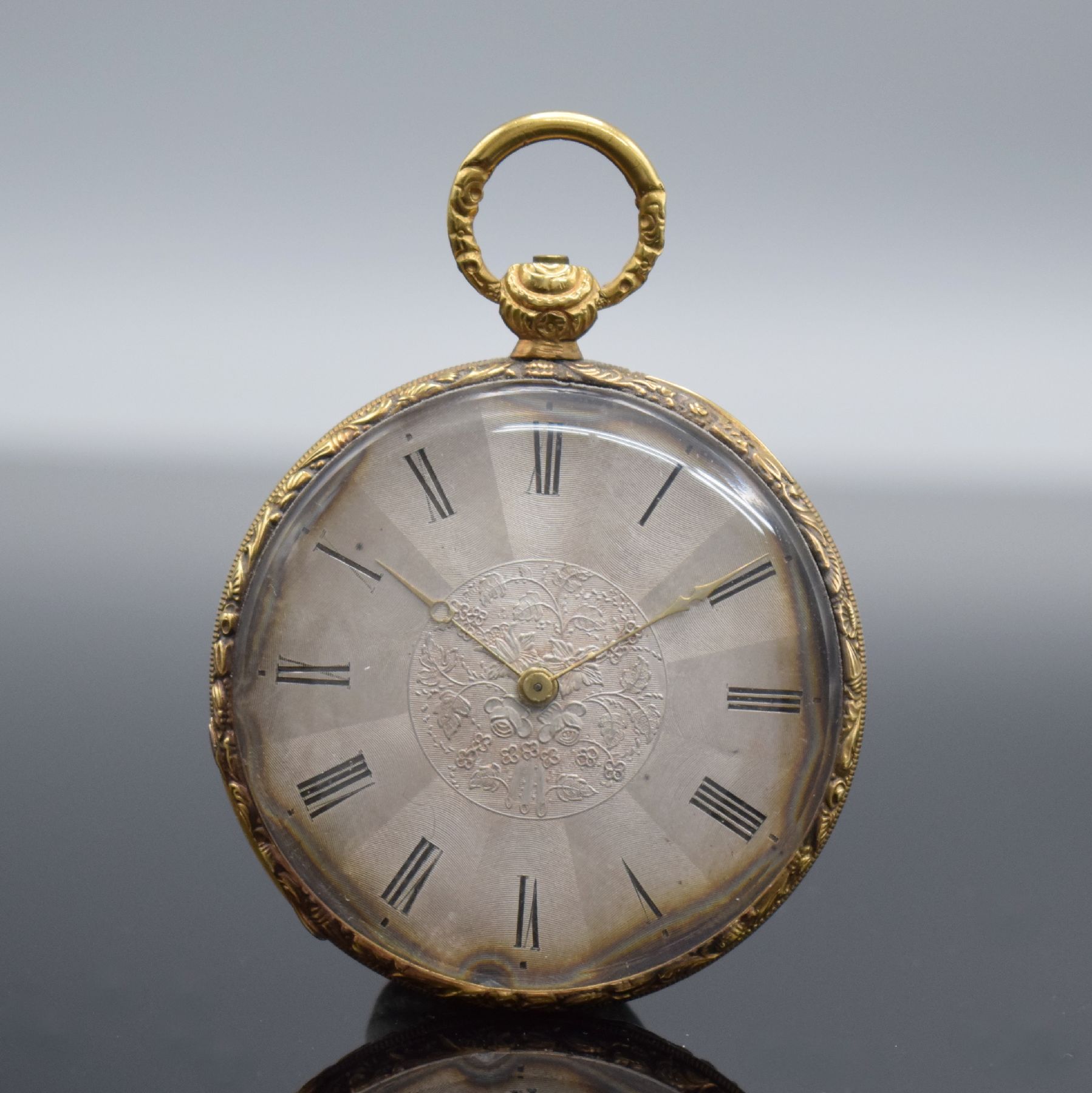 Offene Taschenuhr in GG 750/000, Schweiz um 1850, Metallcuvette, floral grav. Ränder, guill. Rückseite, silb. Zifferbl. m. röm. Zahlen z. T. ...