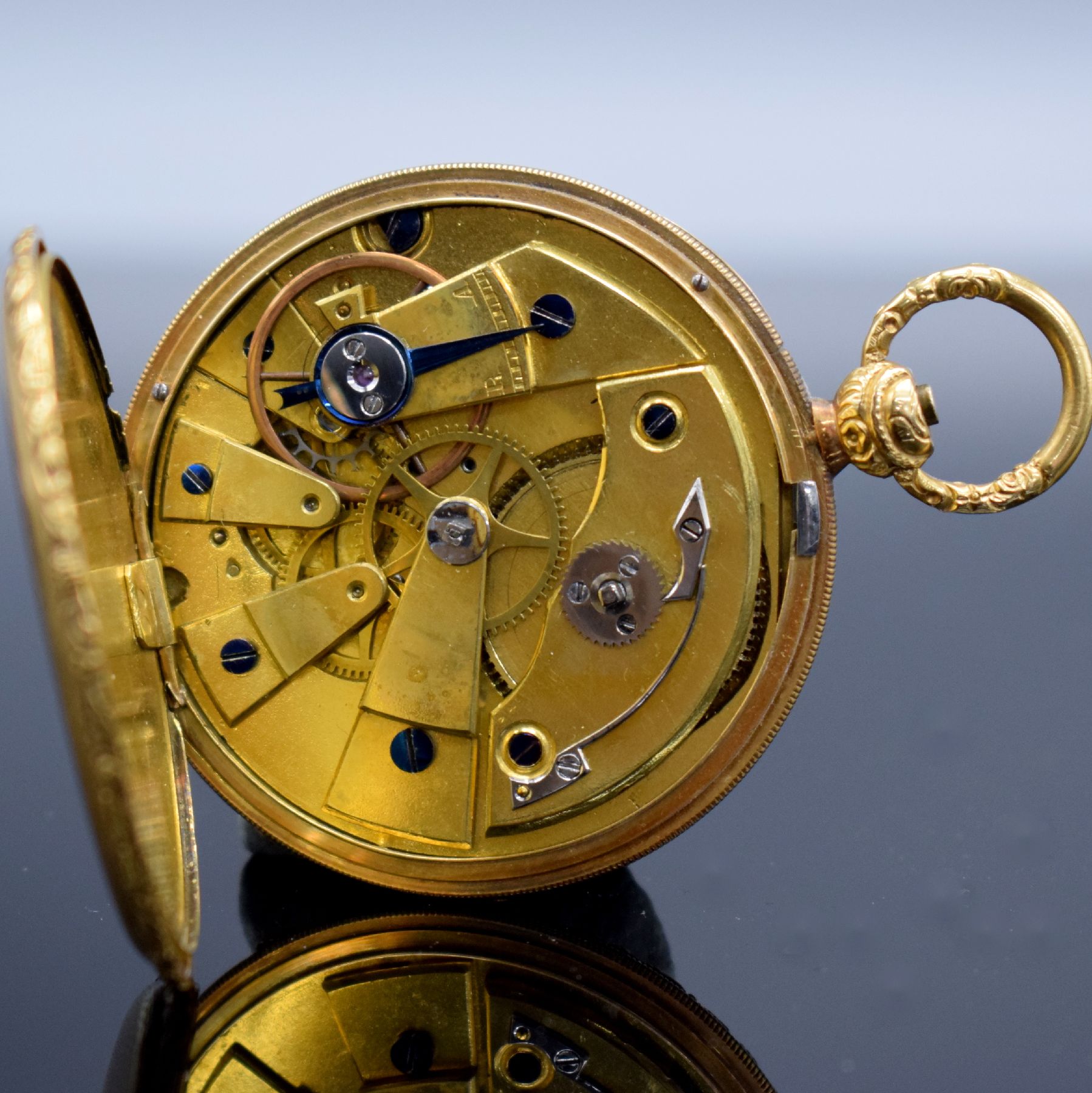 Detail e: Offene Taschenuhr in GG 750/000, Schweiz um 1850, Metallcuvette, floral grav. Ränder, guill. Rückseite, silb. Zifferbl. m. röm. Zahlen z. T. ...