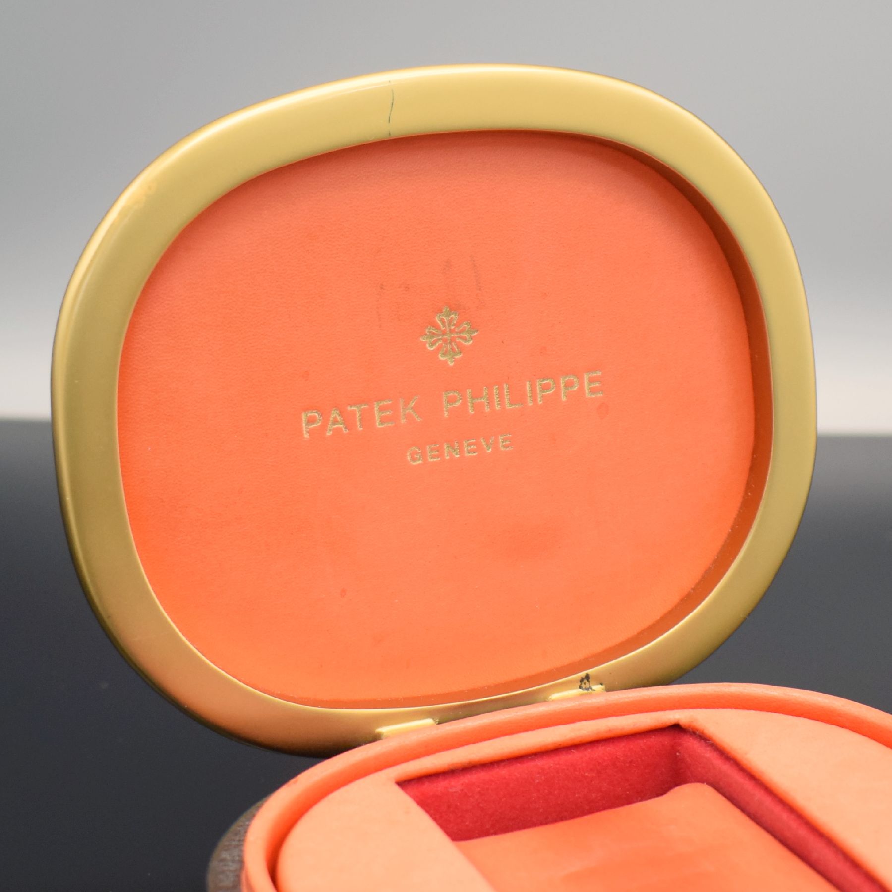 Detail b: PATEK PHILIPPE Ellipse-förmige Uhrenbox in schwarzem Leder, 1970er Jahre, gold. Rand, innen rotes Leder, M. ca. 6 x 13 x 11 cm, voll nutzbar