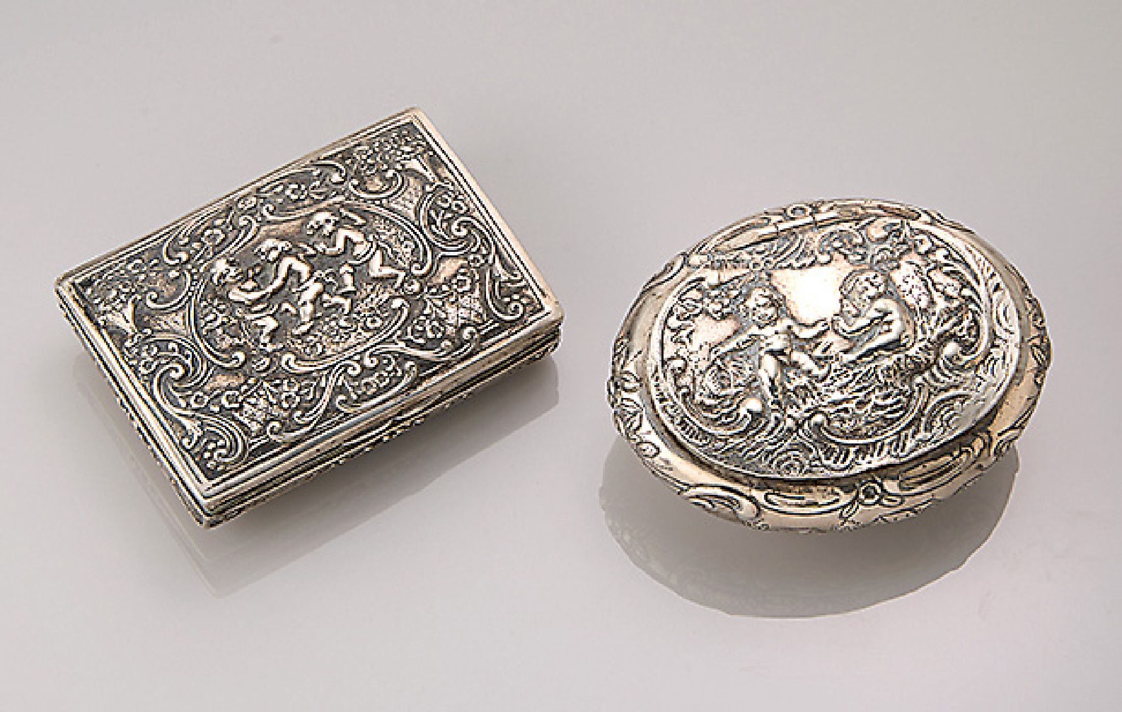 Konvolut 2 Silberdosen Hanau, um 1900, reich verziert mit Puttendekor, 1 x oval ca. 8 x 6 cm, rücks. Monogr. und bez. Kreuznach 1895, 1 x 8 x 5.5 ...