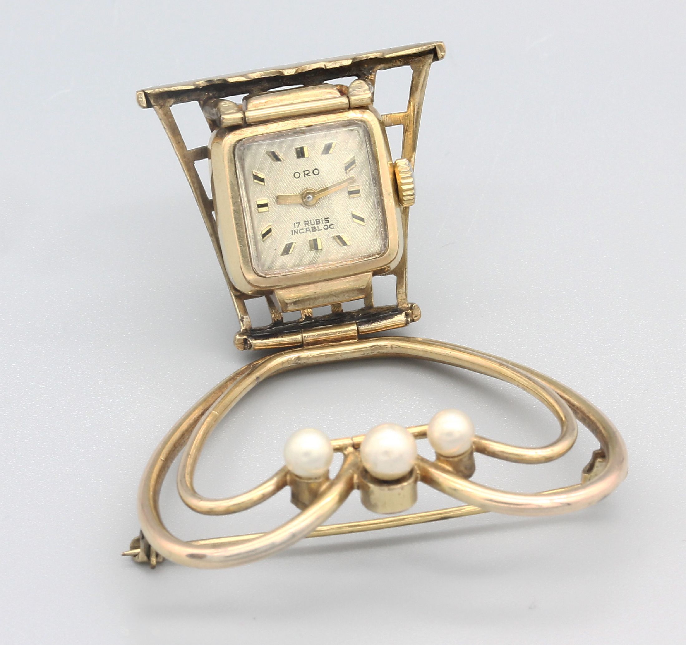 Detail a: Broschenuhr, 1950er Jahre, Metall vergoldet, Zifferbl. bez. Oro, 17 St., Incabloc, Ausklappmechanismus bewirkt Nutzung als kleine Tischuhr, ...