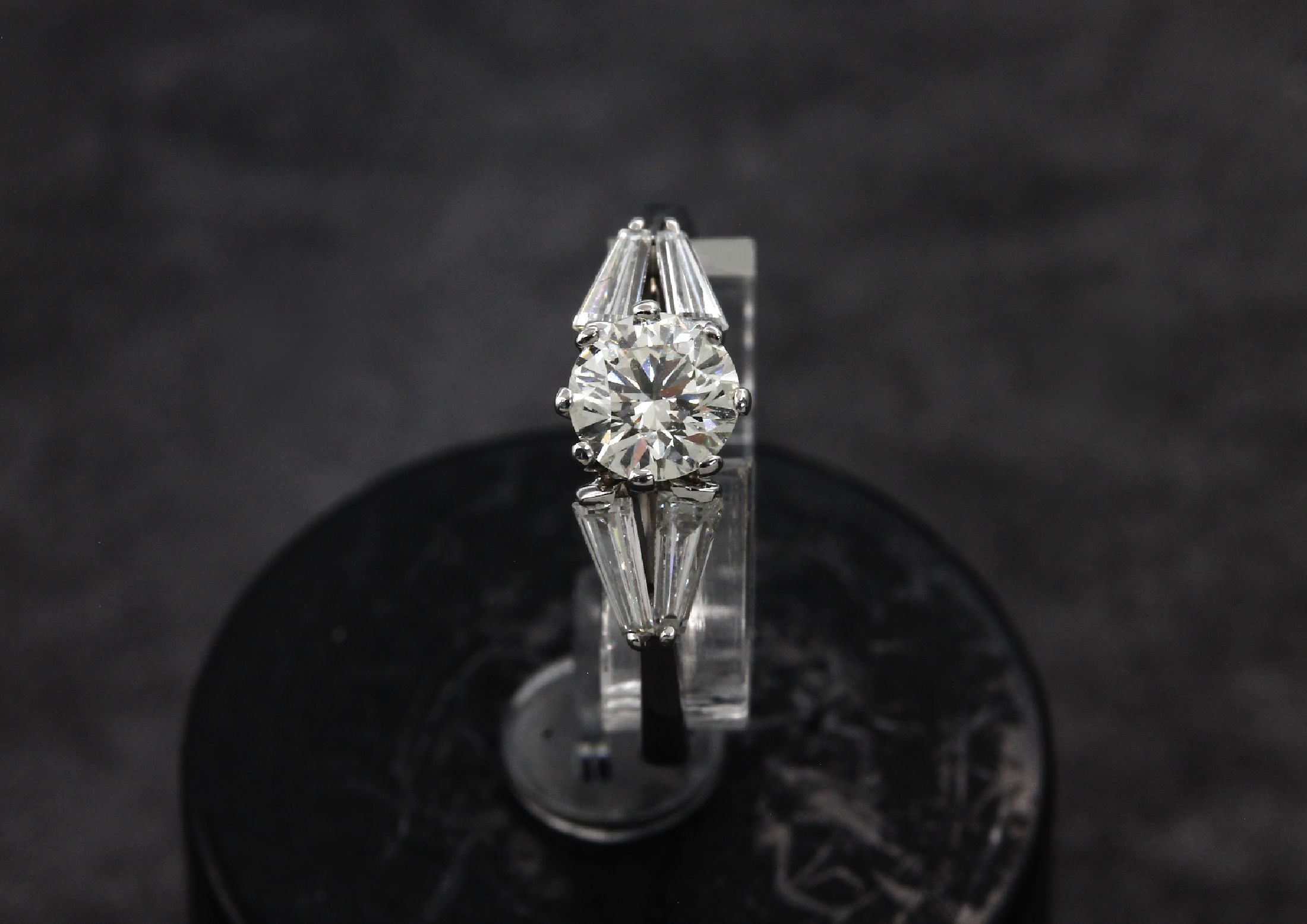 Detail a: 18 kt Gold Diamant-Ring, WG 750/000, 1 Brillant ca. 0.60 ct get. Weiß/si, 4 Diamant -Trapeze zus. ca. 0.50 ct Weiß/ vs, total ca. 1.10 ct get. ...