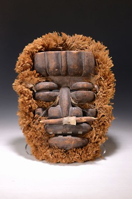 Image 26622315 - Face mask, Bete, Ivory Coast, 20th century, softwood, carved, metal teeth, slit and protruding eye area, domed forehead, fur-like fiber wreath, traces of age, h. 45 cm