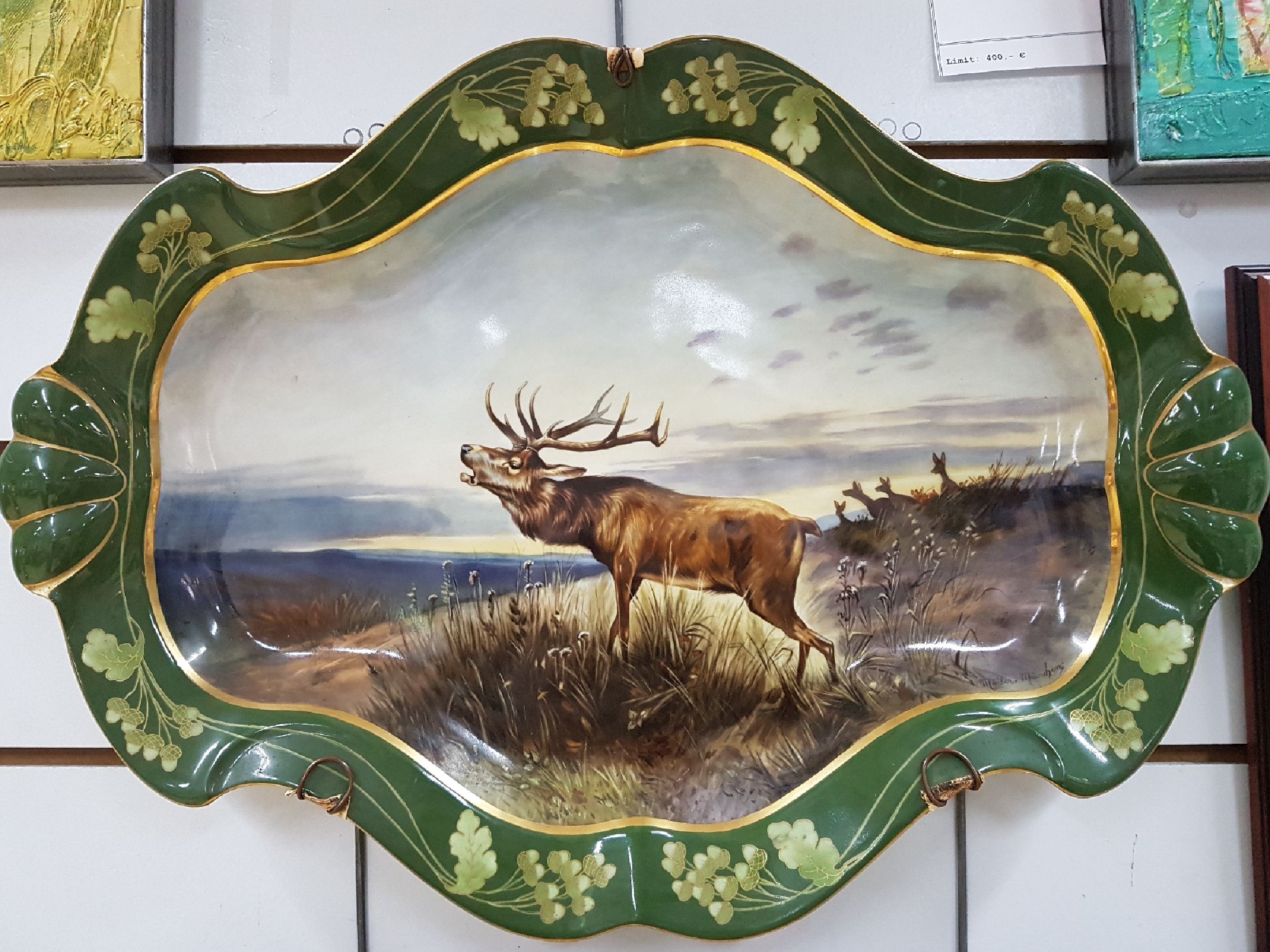 Detail a: Große ovale Platte, Nymphenburg, um 1900, reich bunt handbemalt mit röhrendem Hirsch in Landschaft, Rand mit goldenem Eichenlaub auf grünem Grund, ...