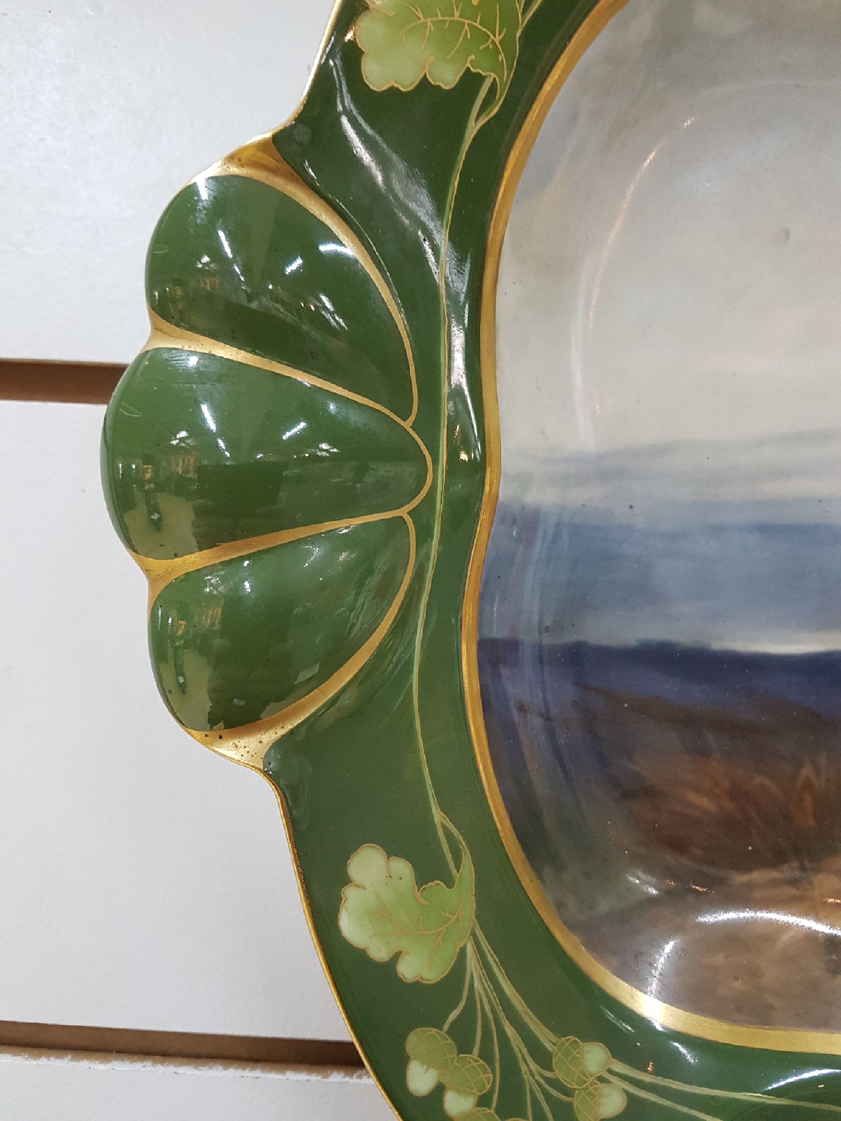 Detail c: Große ovale Platte, Nymphenburg, um 1900, reich bunt handbemalt mit röhrendem Hirsch in Landschaft, Rand mit goldenem Eichenlaub auf grünem Grund, ...