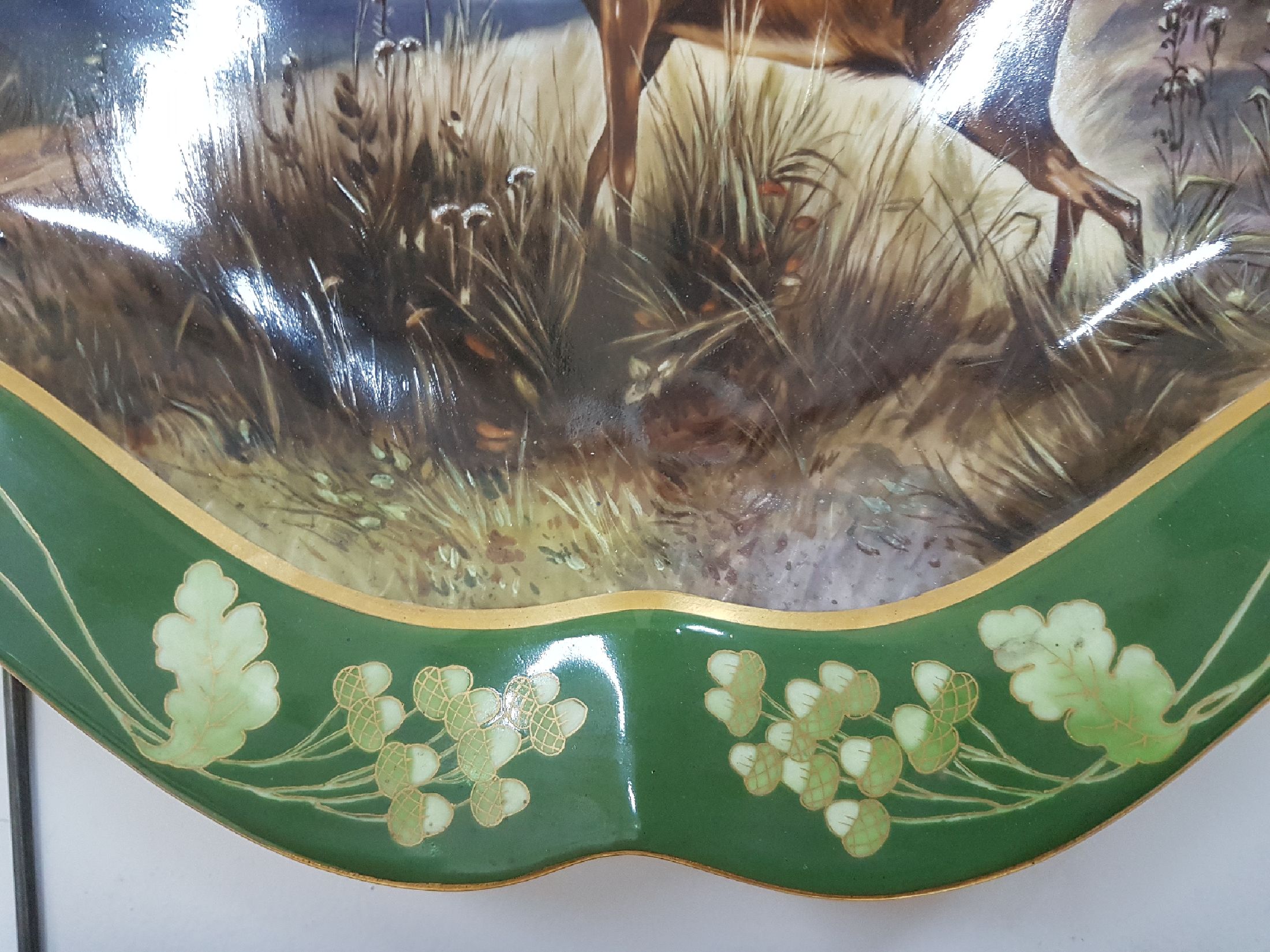 Detail d: Große ovale Platte, Nymphenburg, um 1900, reich bunt handbemalt mit röhrendem Hirsch in Landschaft, Rand mit goldenem Eichenlaub auf grünem Grund, ...