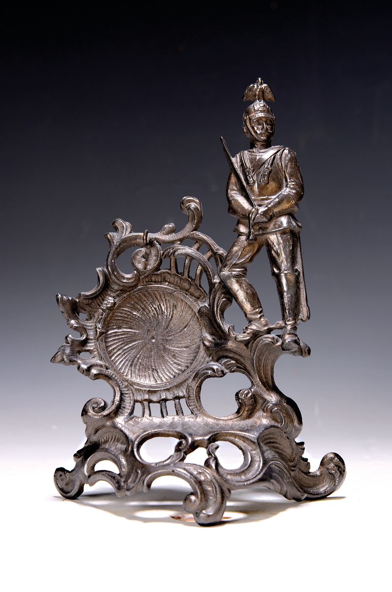 Taschenuhrenständer, deutsch, um 1880-90, Metallguß mit Rocaillendekor und Soldatenfigur seitlich, H. ca. 19.5cm