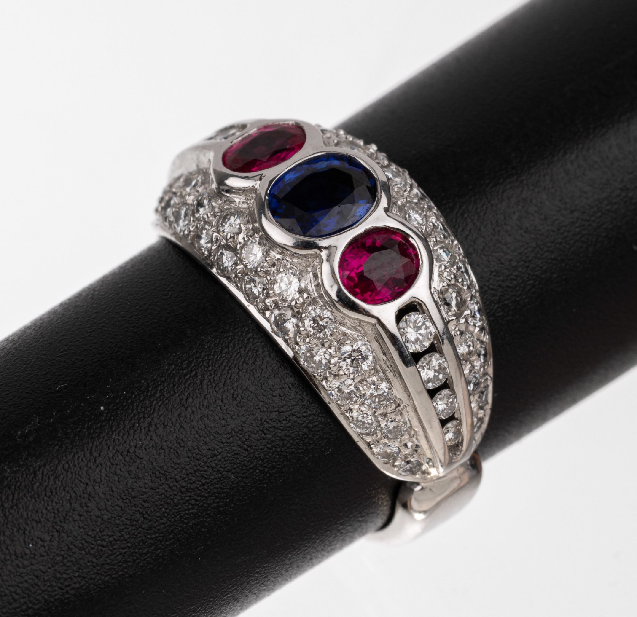 18 kt Gold Saphir Farbstein Ring, WG 750/000, 1 ovalfacett. Saphir ca. 0.54 ct, 2 ovalfacett. Rubine zus. ca. 0.56 ct, 58 Brillanten zus. ca. 0.82 ...