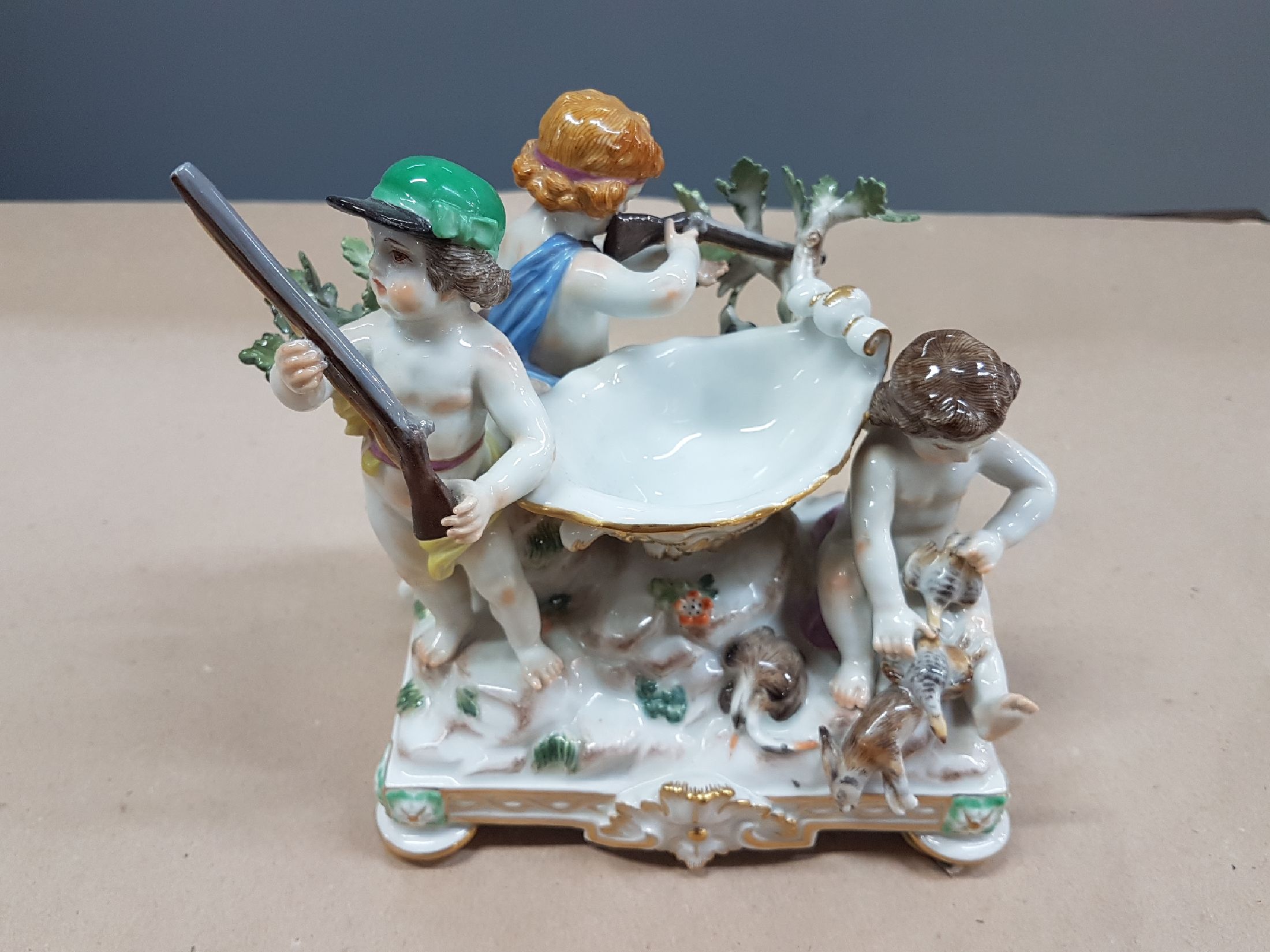 Detail a: Seltener Tafelaufsatz mit Putten, Meissen, um 1900, zentrale Muschelschale auf Felsen, umgeben von drei Putten mit jagdlichen Attributen: zwei mit ...