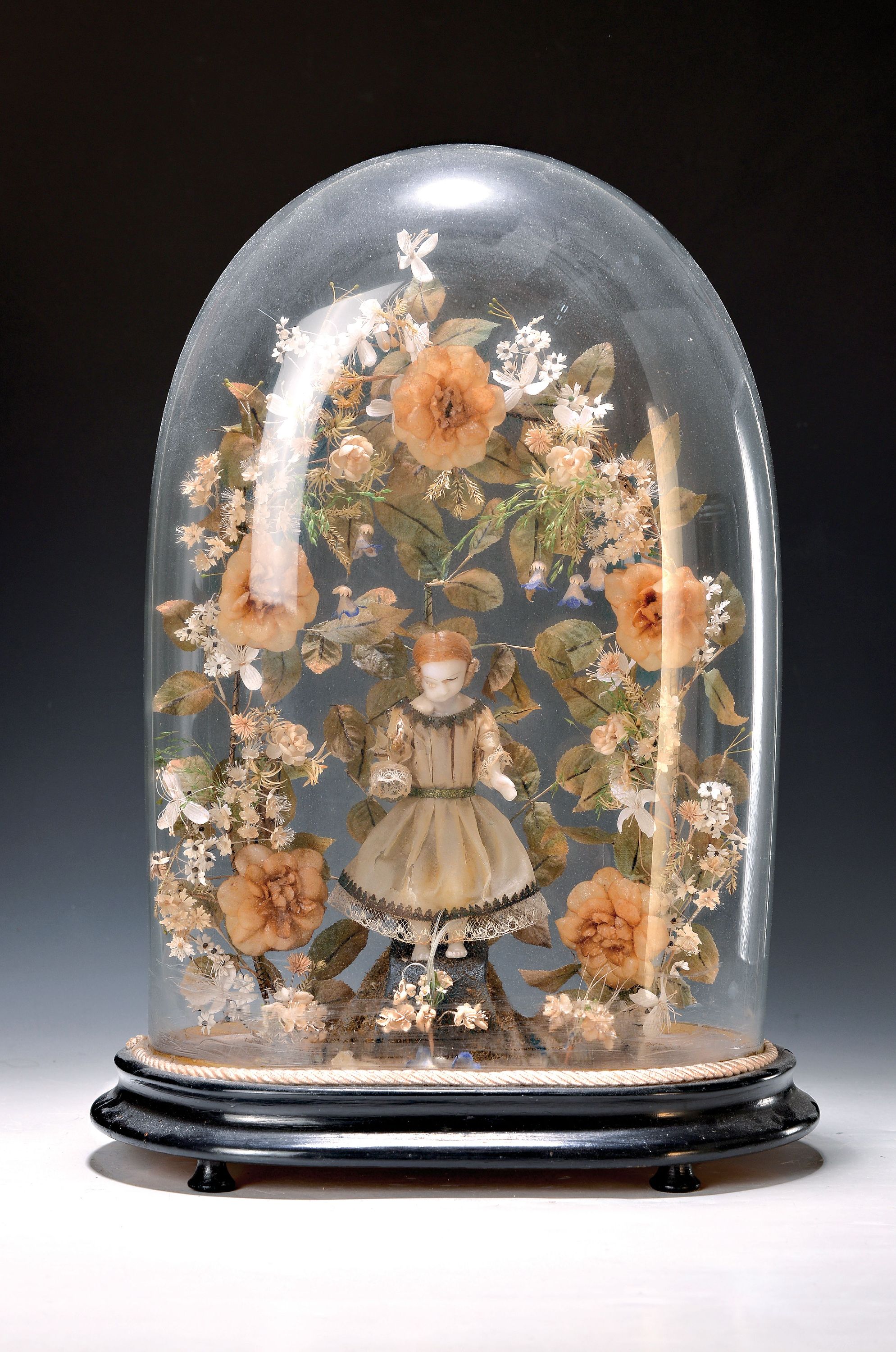 Eingericht, süddeutsch, 19. Jh., mittig Wachspuppe (besch.), feiner Kranz aus Blüten und Blättern aus Stoffen und Papier, orig. Glasdom und ...
