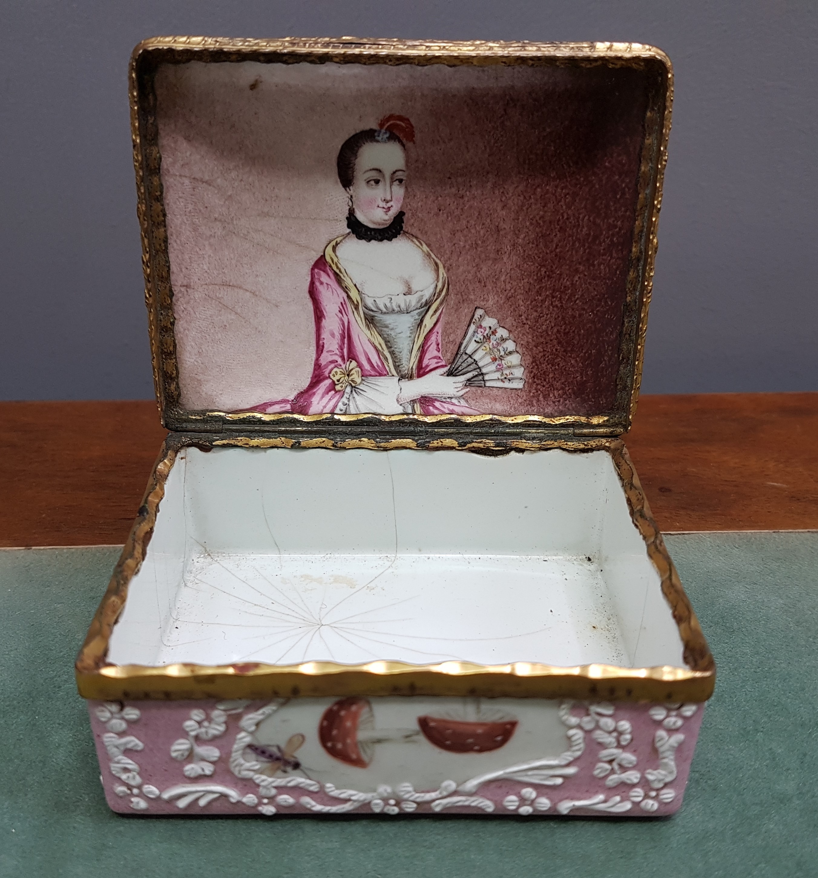 Detail d: Deckeldose, Frankreich, 19. Jh., Metall fein emailliert in rosa mit weißen aufgelegten Ornamenten, in Kartuschen Emailmalerei von Apfel, Pilzen, ...