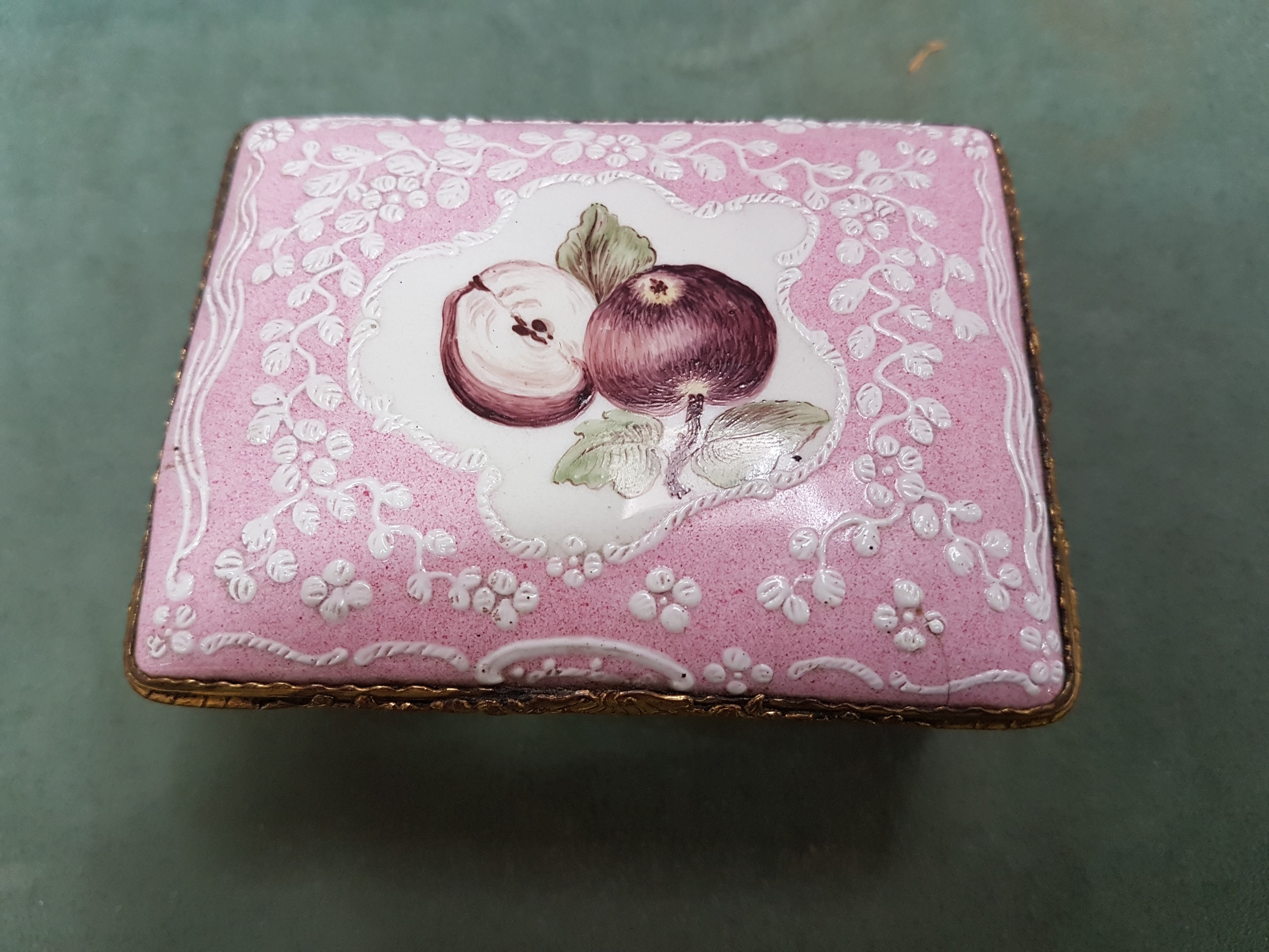 Detail g: Deckeldose, Frankreich, 19. Jh., Metall fein emailliert in rosa mit weißen aufgelegten Ornamenten, in Kartuschen Emailmalerei von Apfel, Pilzen, ...