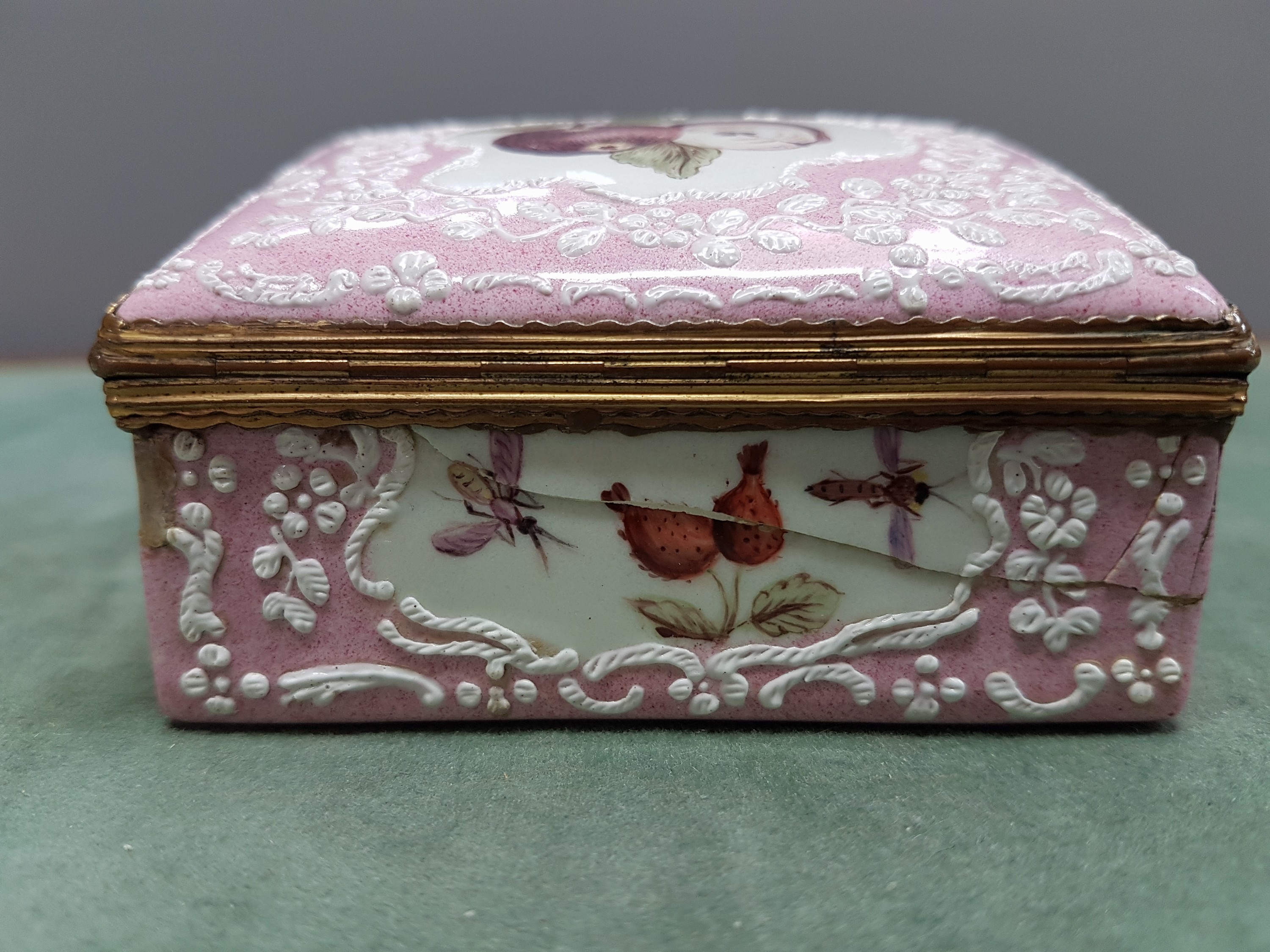 Detail i: Deckeldose, Frankreich, 19. Jh., Metall fein emailliert in rosa mit weißen aufgelegten Ornamenten, in Kartuschen Emailmalerei von Apfel, Pilzen, ...