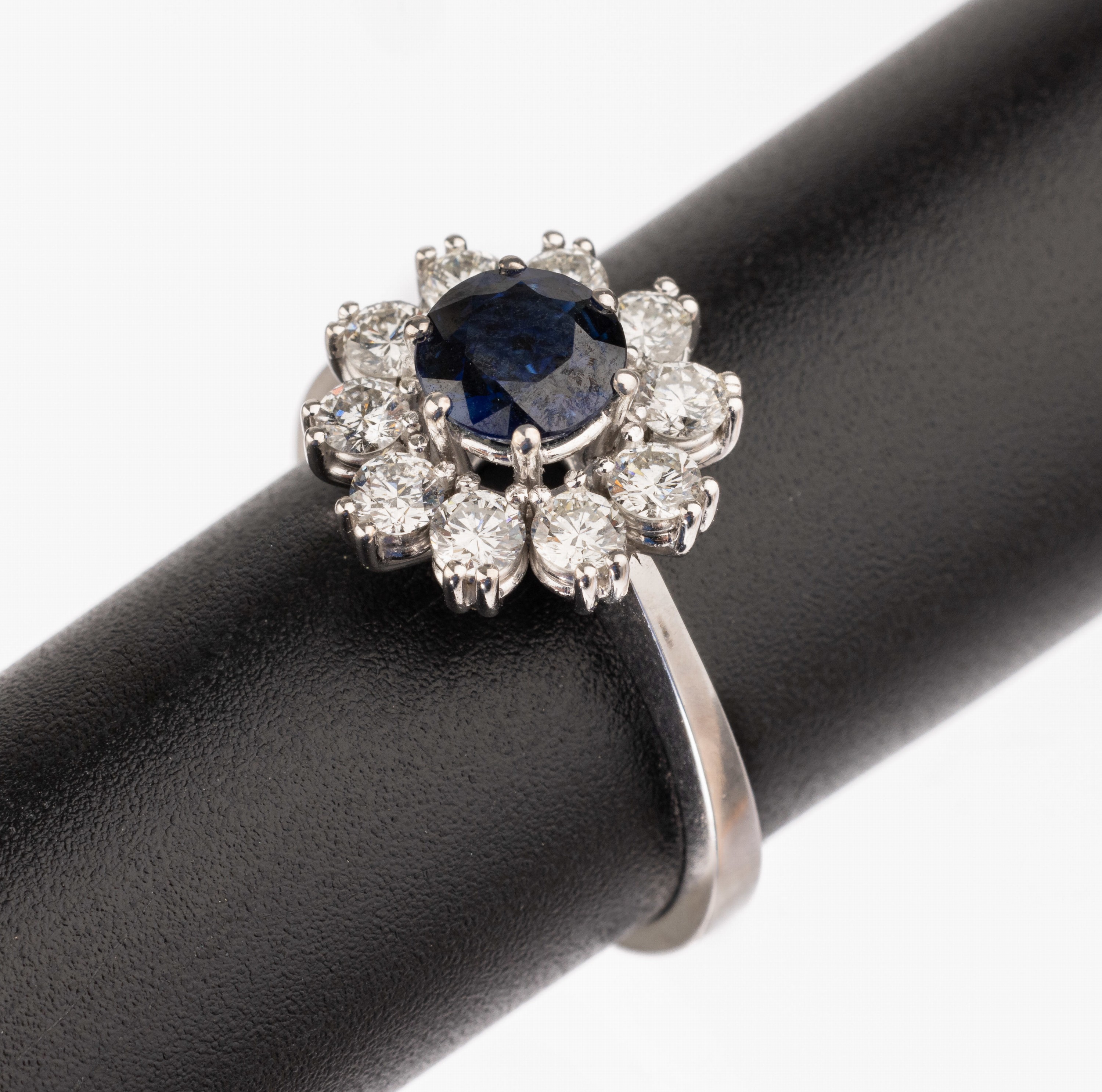 18 kt Gold Saphir-Brillant-Ring, WG 750/000, mittig erhaben gefasster rundfacett. Saphir ca. 0.98 ct, umgeben von 10 Brillanten zus. ca. 0.74 ct ...