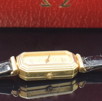 26745572a - OMEGA De Ville diamantbesetzte Damenarmbanduhr in GG 585/000, Schweiz um 1980, quartz, Baguette-förm., 8-eck. Geh., anges. Anstöße, getreppte Lünette, Boden aufgedr., gold. Zifferbl. fl., schwarze Zeiger, Omega-Box anbei, M. ca. 29 x 13 mm, EZ 2-3