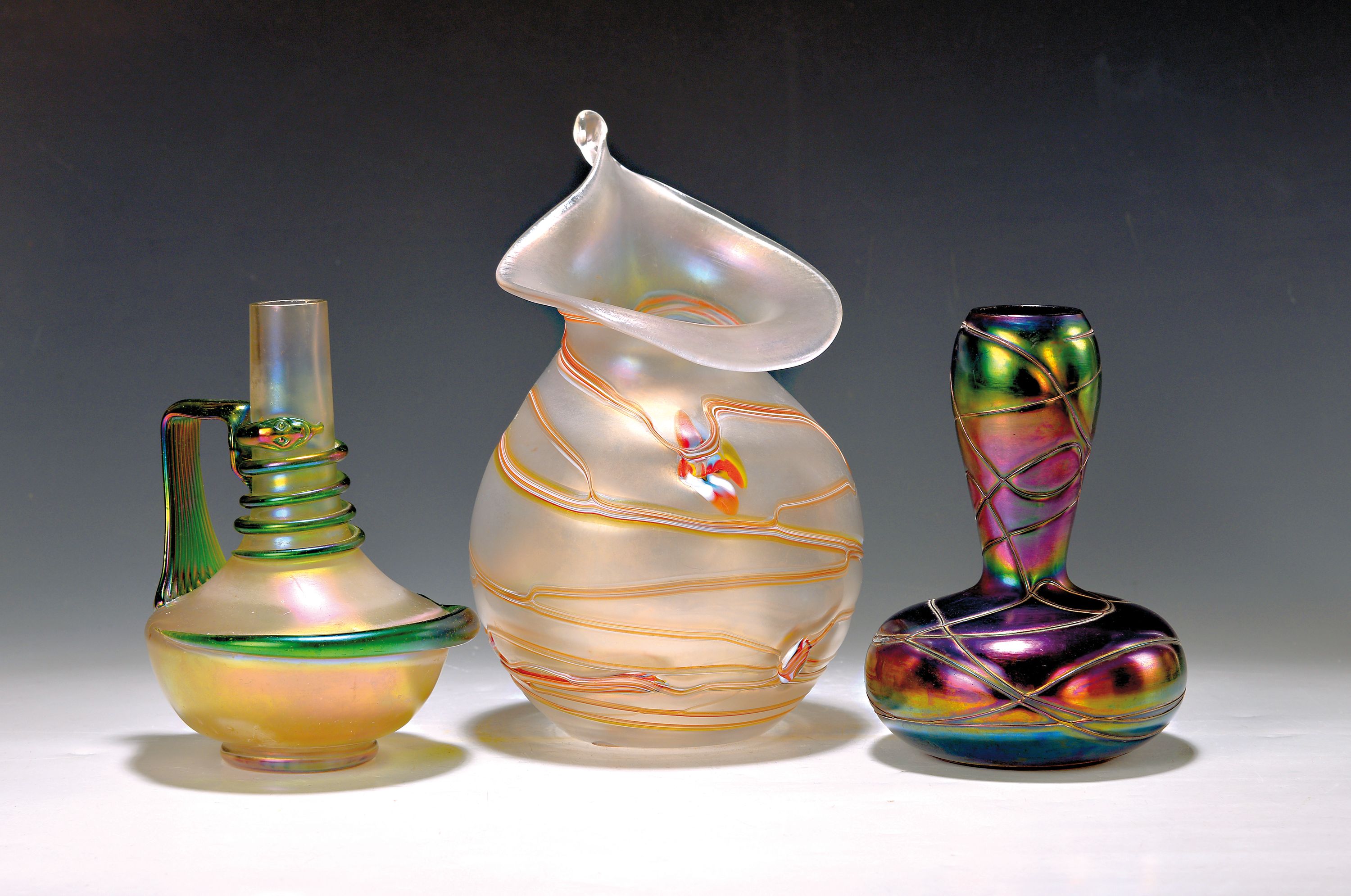 3 Ziervasen, Böhmen, wohl Pallme König, Anfang 20.Jh., Glas, 1x mit Fadenaufschmelzungen und violett irisierend H. 18 cm; 1x mit grünen ...