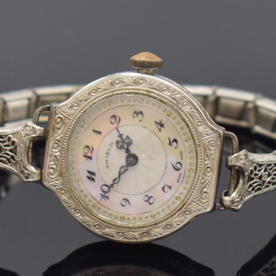 26768675a - WALTHAM white gold-Filled wristwatch model Sapphire, manual winding, USA around 1930, partial engine-turned dial with mother-of- pearl inlay marked Shield, hinge case, case back with monogram, case lavish engraved, lavish pierced and engraved stretch-bracelet with case lock, compensation-balance with Breguet-hairspring, pressed chatons, diameter approx. 27 mm, length approx. 16,5 cm, condition 2-3
