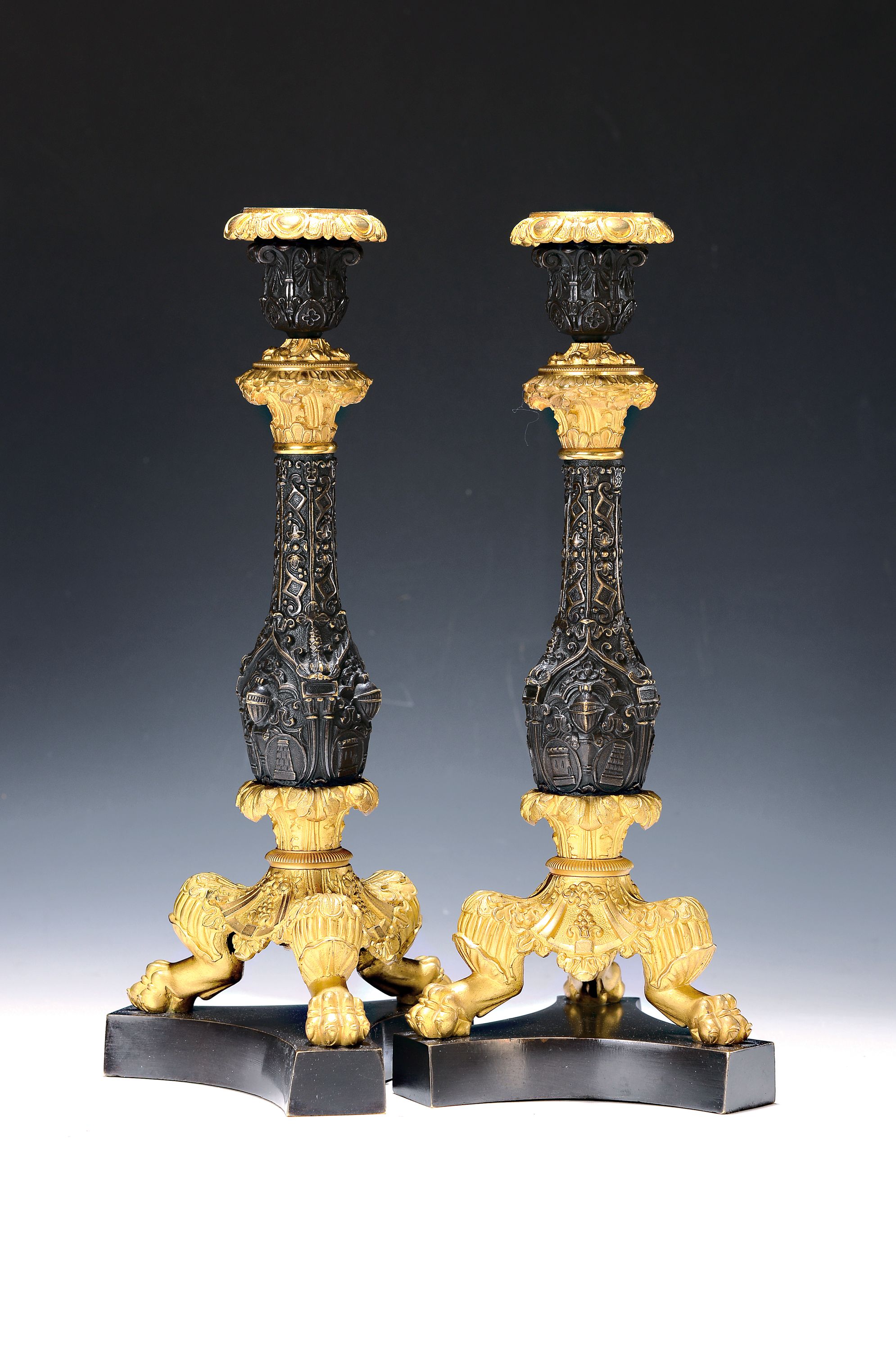 Paar Kerzenleuchter, Frankreich, um 1820-30, reich reliefierter Bronzeguß z.T. vergoldet, auf drei Klauenfüßen stehend, Maskerone von Rittern, ...
