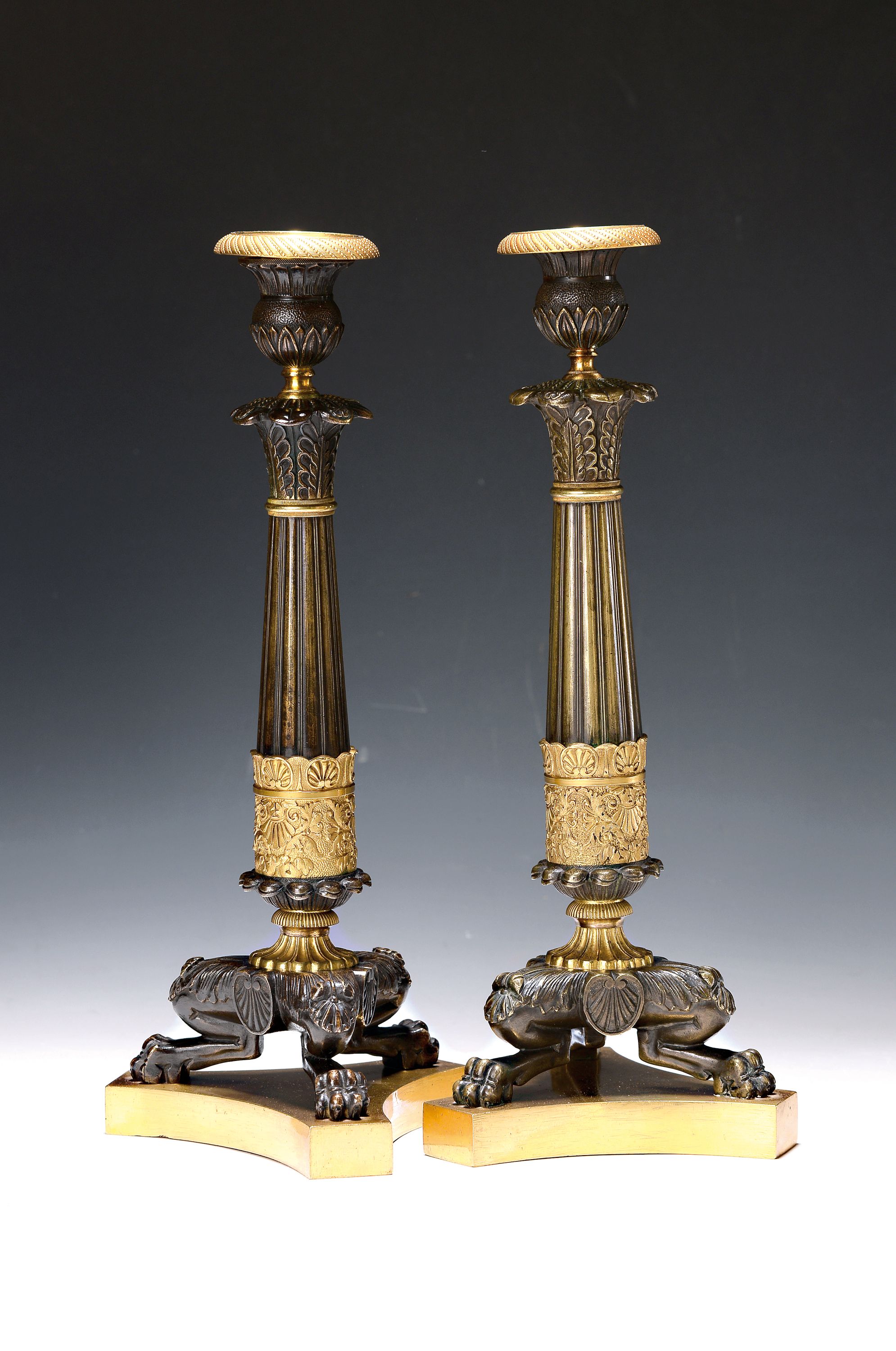 Paar Kerzenleuchter, Frankreich, um 1820-30, reich reliefierter Bronzeguß z.T. vergoldet, auf drei Klauenfüßen stehend, kannelierte Säulen mit ...