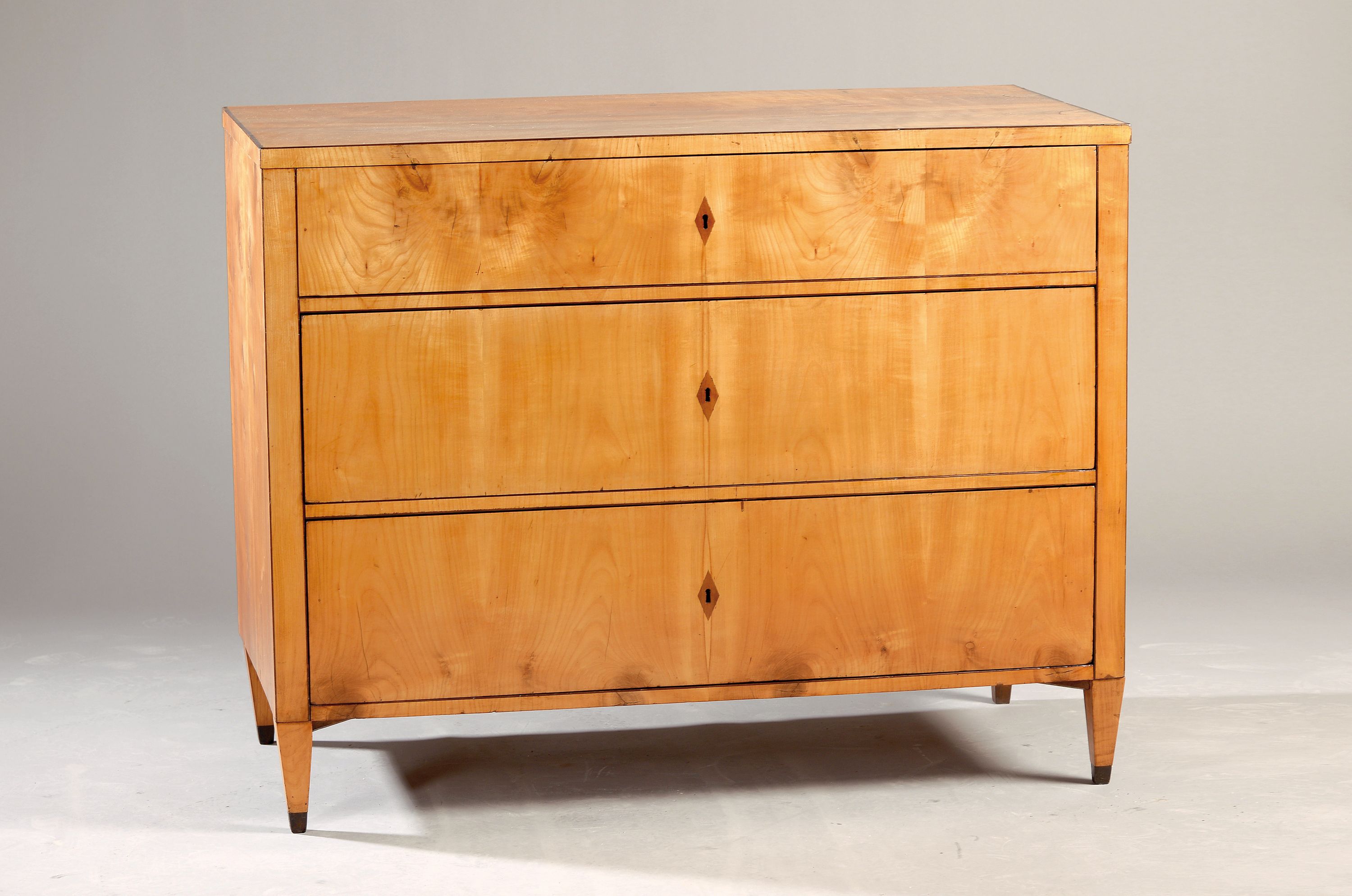 Biedermeier-Kommode, um 1825/30, Kirschbaumfurnier, Korpus mit 3 Schubladen, Bandintarsien, auf spitzen Füßen, 2 Schlüssel, ca. 92 x 117 x 58 cm, ...