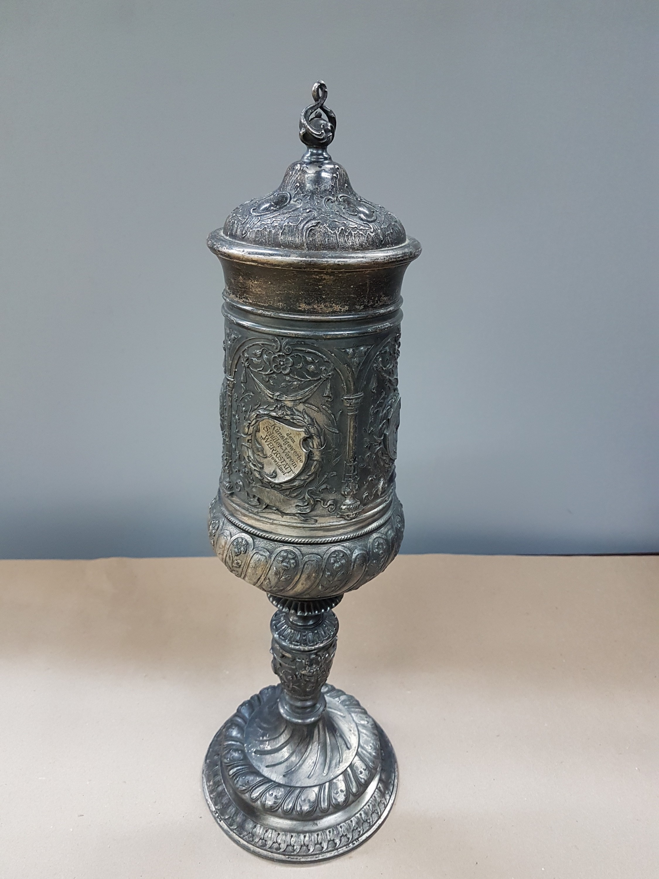 Detail b: Deckelpokal, deutsch, WMF, um 1890, Legierung I/O, reich reliefiert mit Akanthus, Palmetten und Ranken, Inschrift: Viribus Unitis, die Lehrer der ...