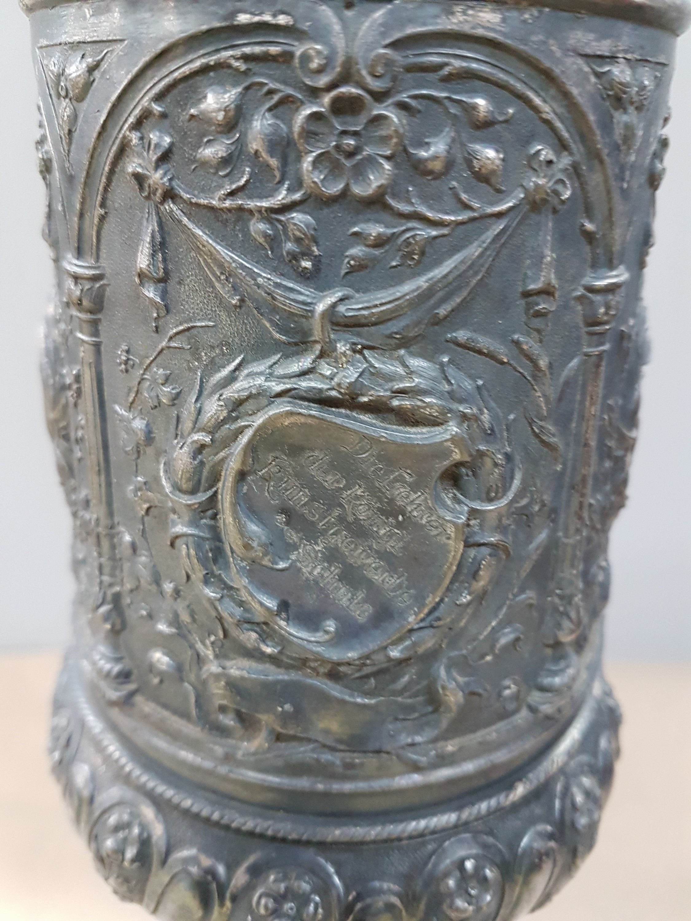 Detail h: Deckelpokal, deutsch, WMF, um 1890, Legierung I/O, reich reliefiert mit Akanthus, Palmetten und Ranken, Inschrift: Viribus Unitis, die Lehrer der ...