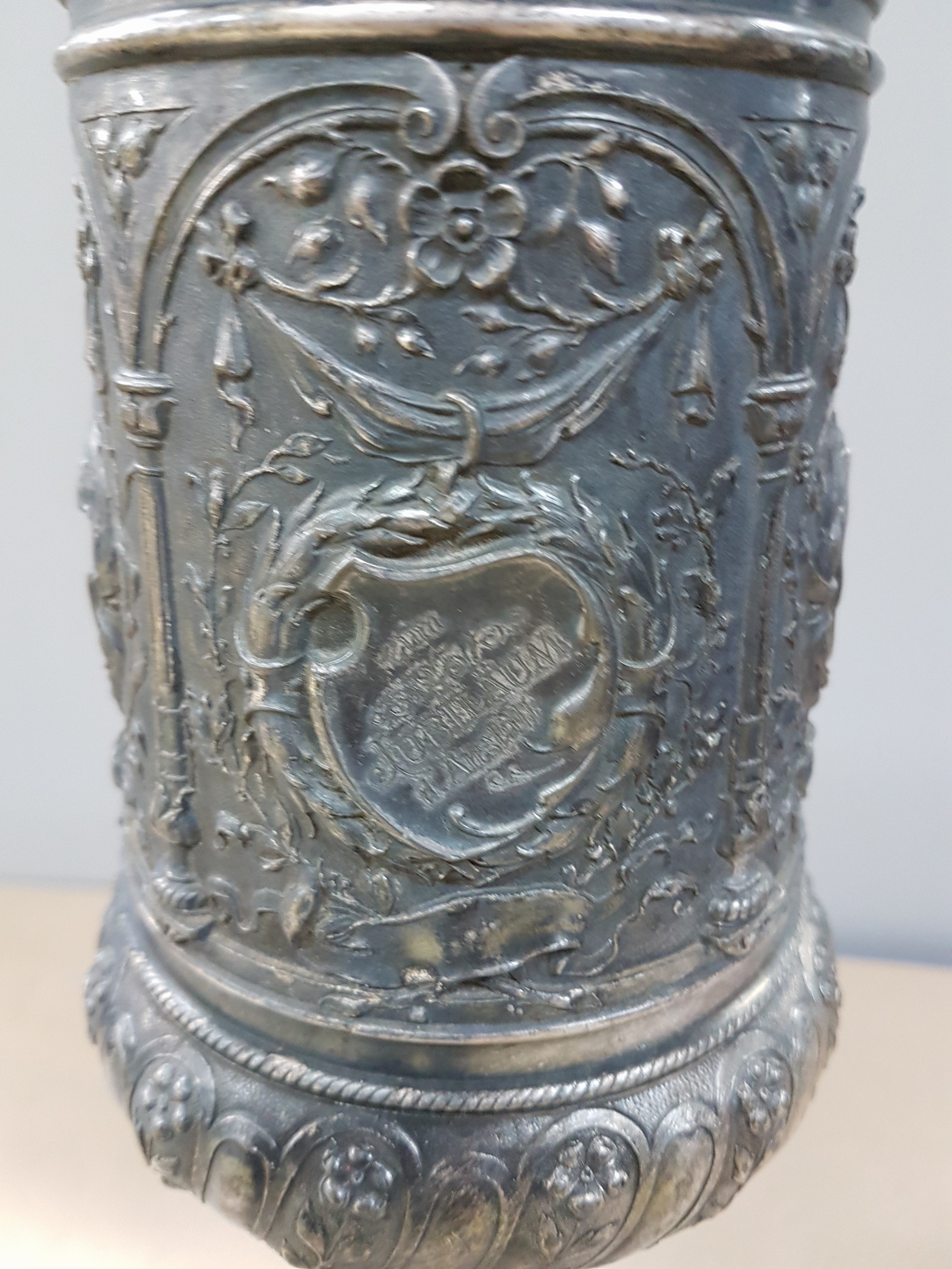Detail i: Deckelpokal, deutsch, WMF, um 1890, Legierung I/O, reich reliefiert mit Akanthus, Palmetten und Ranken, Inschrift: Viribus Unitis, die Lehrer der ...