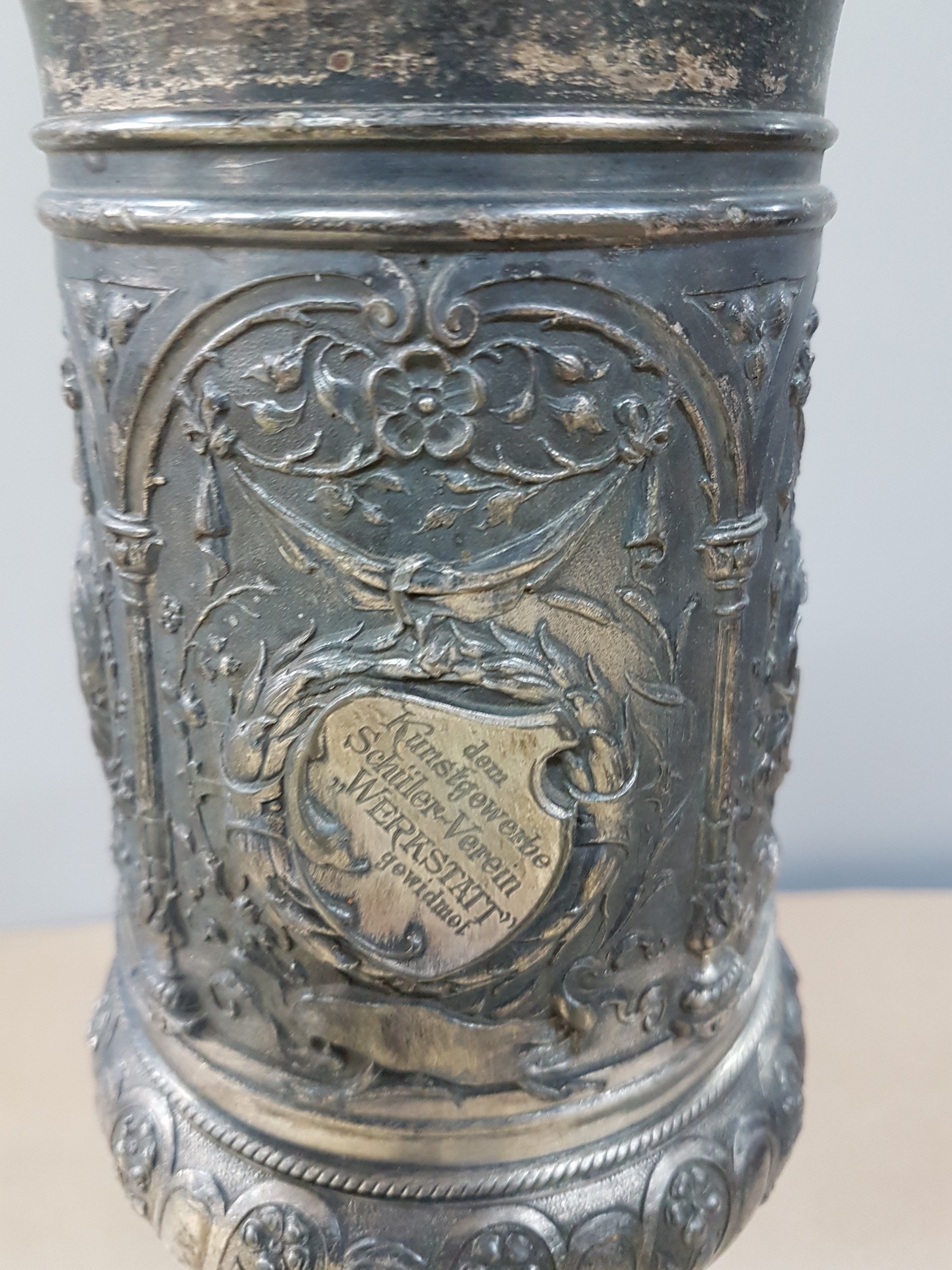 Detail j: Deckelpokal, deutsch, WMF, um 1890, Legierung I/O, reich reliefiert mit Akanthus, Palmetten und Ranken, Inschrift: Viribus Unitis, die Lehrer der ...