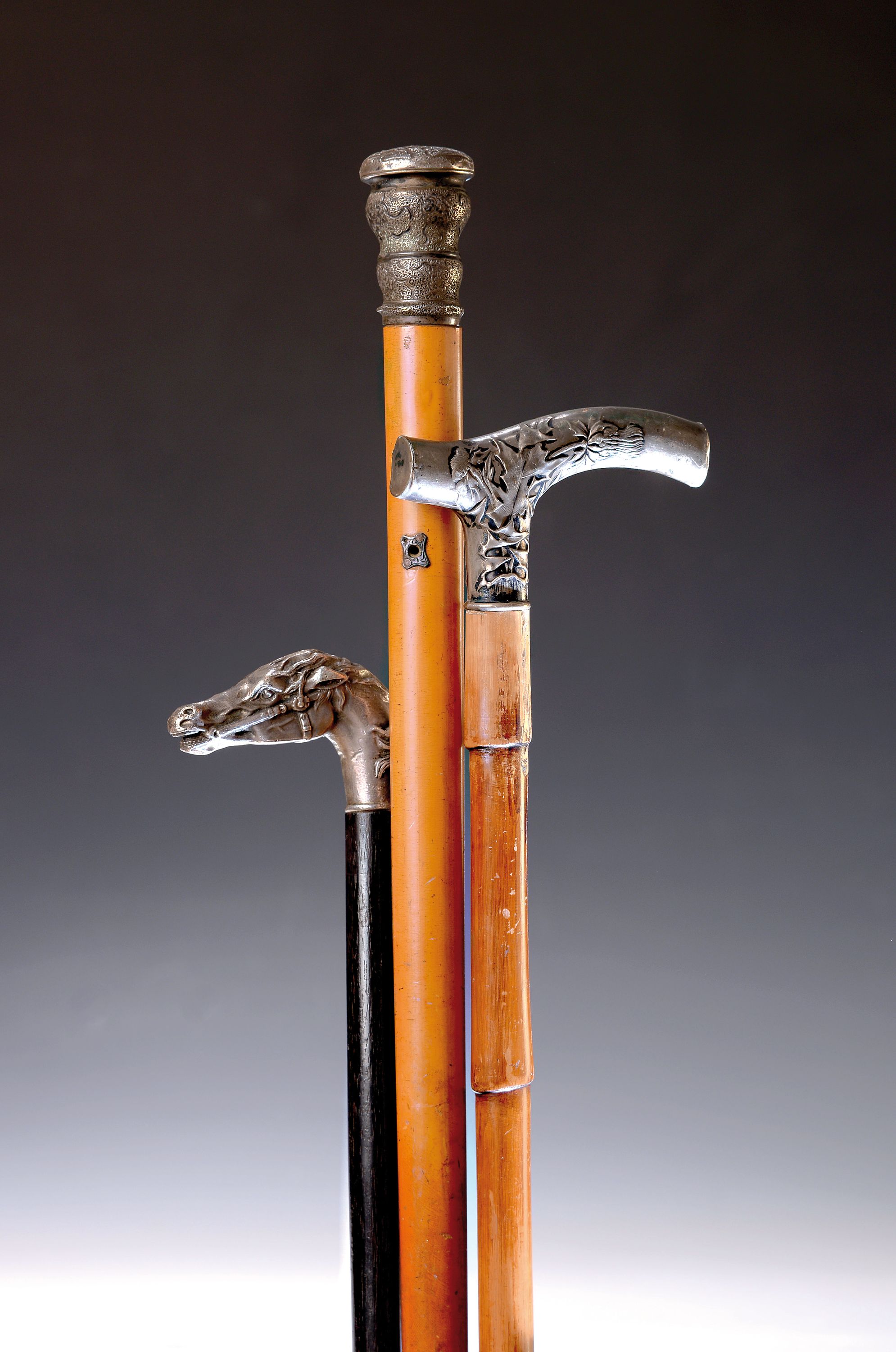 3 Gehstöcke, deutsch, um 1900, je mit Holzschuß, Fritz-Griff 800er-Silber mit Disteldekor (best.) L. 87 cm; Griff als Pferdekopf aus Metall, L. 80 ...
