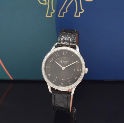 Image HERMES wristwatch series Slim d´Hermes reference CA2.230, stainless steel case including original leather strap with original buckle, bezel lavish with diamonds, quartz, case back screwed-down 4-times, black, in center engine-turned dial with Arabic hour, display of hour & minutes, diameter approx. 32 mm, Hermes storage back enclosed, unworn stock, condition 1-2
