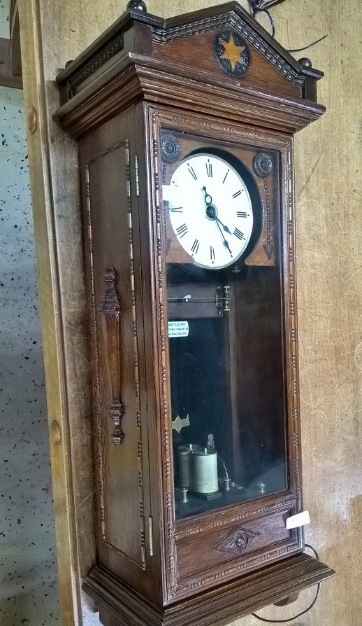 Detail a: Wanduhr, elektrisch, um 1930, Holzgehäuse verziert u. profiliert, sek. lackiert, Giebelabschluss, Türverschluss rechts mittels einzelner ...