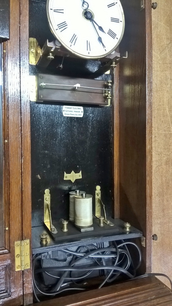 Detail b: Wanduhr, elektrisch, um 1930, Holzgehäuse verziert u. profiliert, sek. lackiert, Giebelabschluss, Türverschluss rechts mittels einzelner ...