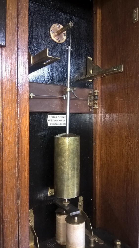 Detail g: Wanduhr, elektrisch, um 1930, Holzgehäuse verziert u. profiliert, sek. lackiert, Giebelabschluss, Türverschluss rechts mittels einzelner ...