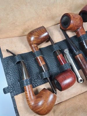 26790376a - Pipe shelf and 22 branded pipes, branded pipes inter alia 5 x Dunhill, Nording, Briar, Bang, 3 x Savinelli, Killarmey, Vauens, Dansk and Peterson, inter alia, in addition one Meerschaum pipe, all used, partly with traces of usage, corner shelf in oak with floral carving, in addition slightly accessories, 84 x 35 cm, Thigh depth 25 cm in addition tobacco vessel, two pipes without mouthpiecee
