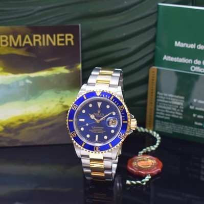 Image ROLEX Oyster Perpetual Submariner reference 16613, self winding, LC 100, V-series, superlative chronometer officially certified in steel/gold combined including oyster bracelet with deployant clasp, blue, unidirectional rast. revolving gold bezel with 60-minutes graduation, sapphire crystal, case back and winding crown screwed down, waterproof from manufacturing, blue dial with rehaut-engraving, applied gilded luminous indices and luminous hands, date under loupe- glass, diameter approx. 40 mm, length approx. 20 cm, original box and papers, condition 2