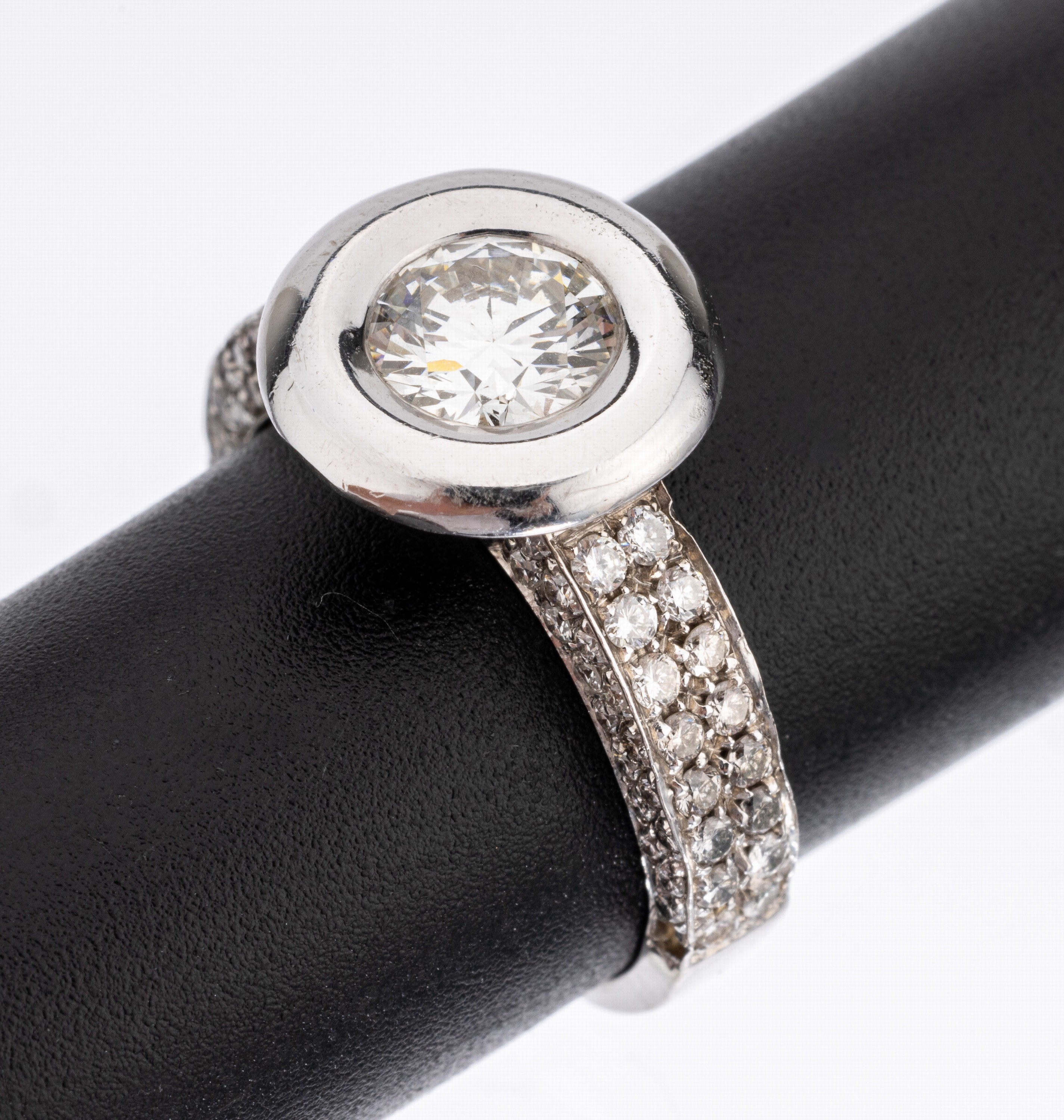 18 kt Gold Brillant-Ring, WG 750/000, mittig Brillant in gr. Zargenfassung ca. 1.0 ct l.get. Weiss/vs, Ringschultern mit 99 Brillanten zus. ca. 0.80 ...