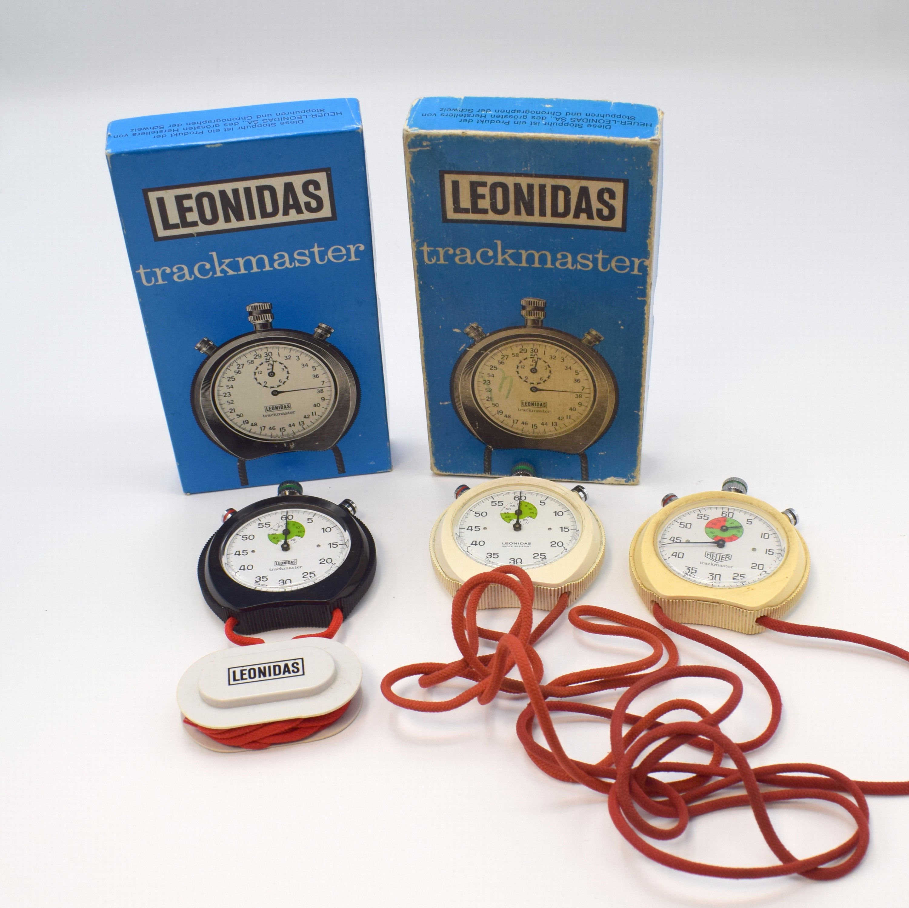 HEUER / LEONIDAS Trackmaster 3 Stoppuhren, Schweiz um 1975, Handaufzug, Kunststoff-Geh. an orig. Kordel, 2 x Leonidas m. orig. Box, separate Drücker ...
