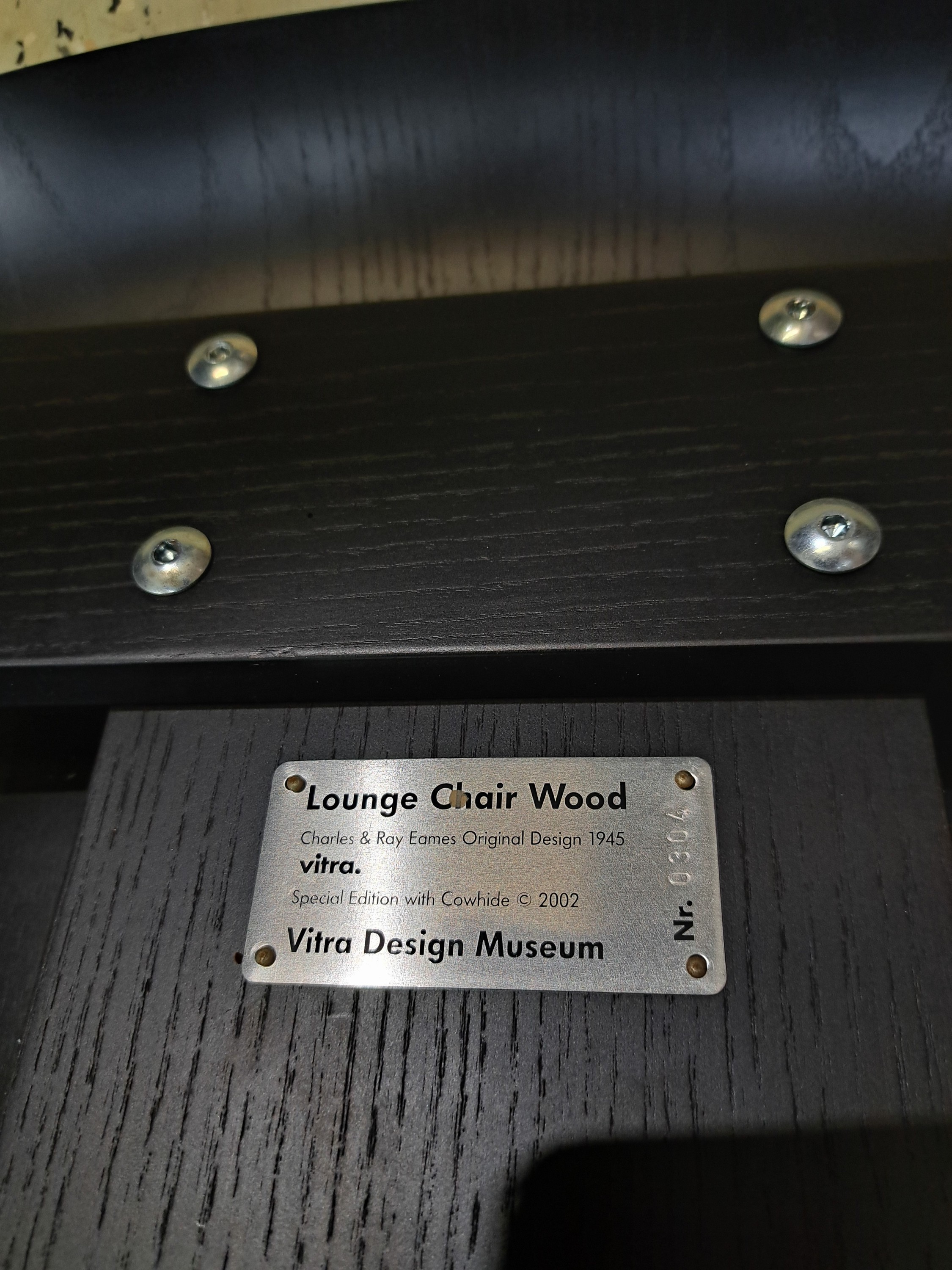 Detail c: Lounge Chair Wood, von Charles Eames, Entwurf 1945, Design Vitra, Schichtholz schwarz lackiert, Kuhfellbezug, Herstelleretikett unter dem Sitz diese ...