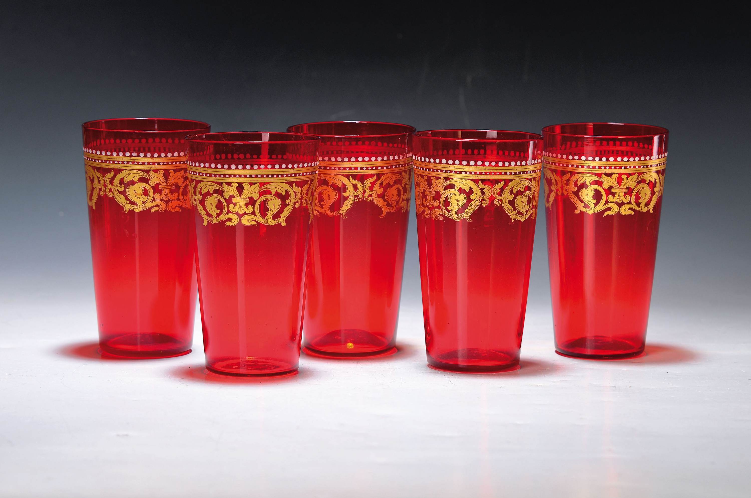 8 Bechergläser, wohl Böhmen, Anfang 20.Jh., rubinrot eingefärbtes Glas, optisch geblasen, historisierender Golddekor, weiß getupfter Kugelfries, ...