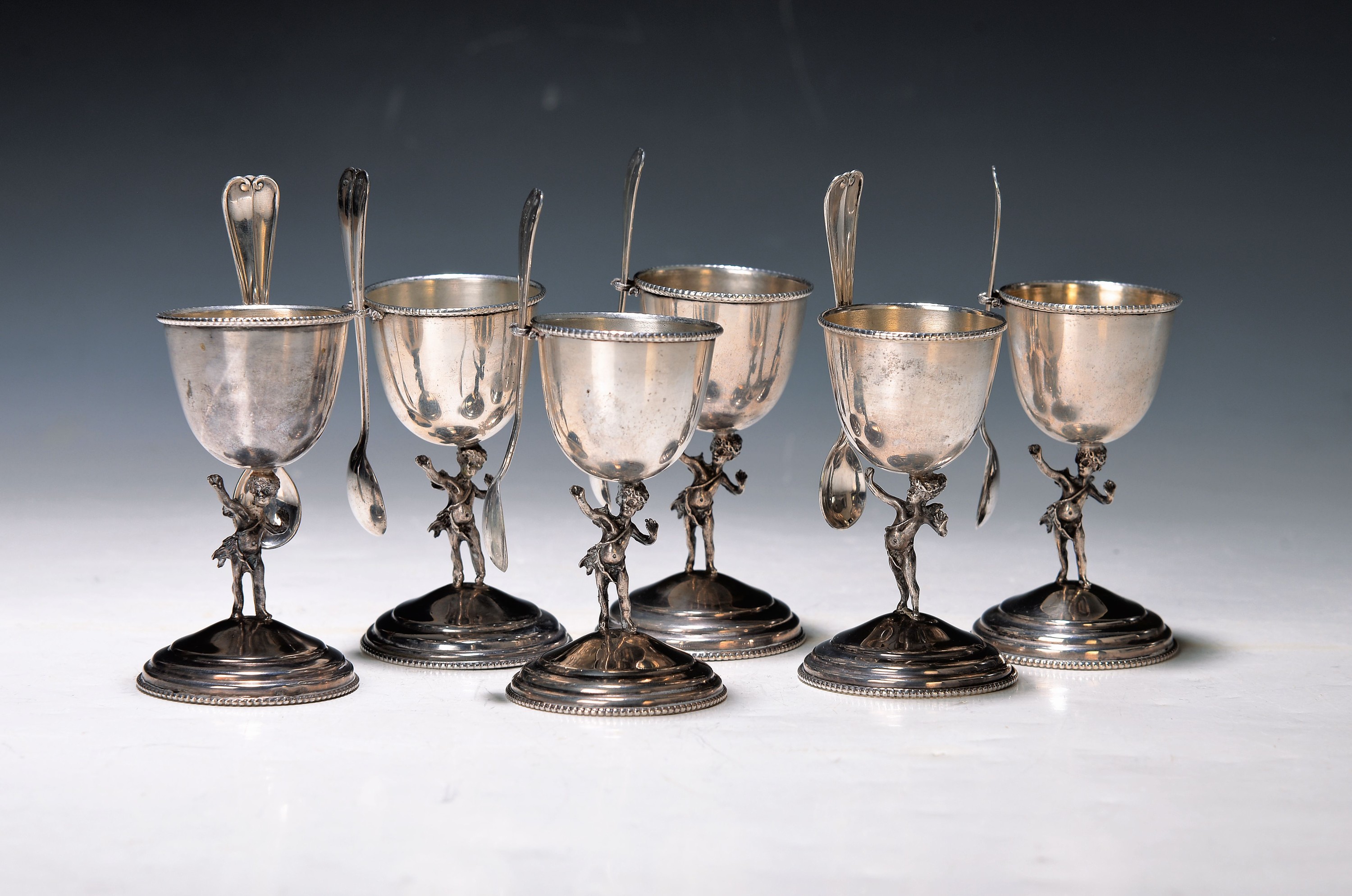 6 SIlber-Eierbecher mit Löffel, um 1900, 800er-Silber, mit vollplastischen Amoretten als Stil, H. ca. 9 cm, mit eingesteckten, Löffelchen 12 cm, am ...