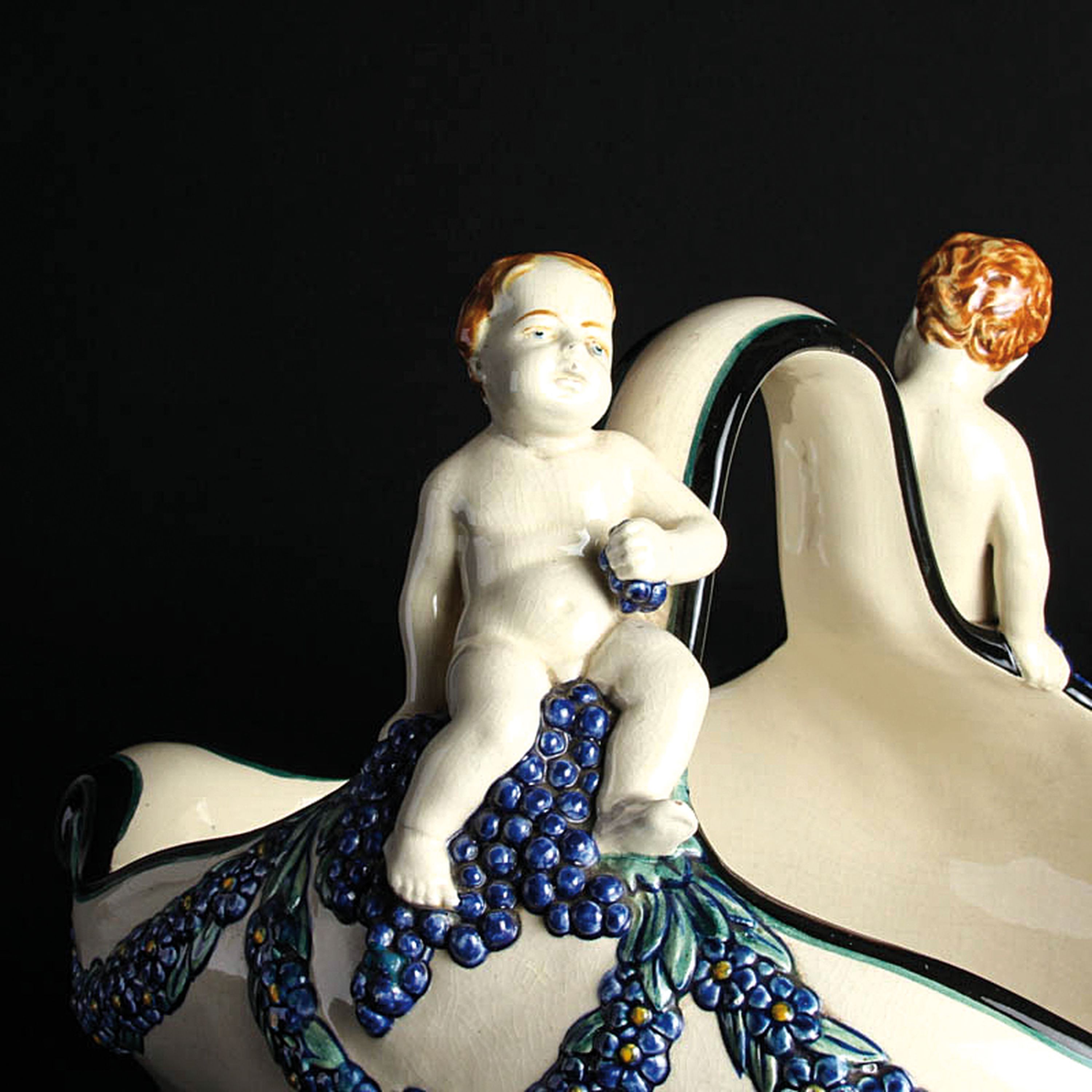 Detail a: Henkelschale mit Traubenputti, Karlsruher Majolika, Entw. Wilhelm Süß (1861-1933), Modellnr. 1164, Keramik, farbig staffiert, Blumenghirlanden und ...