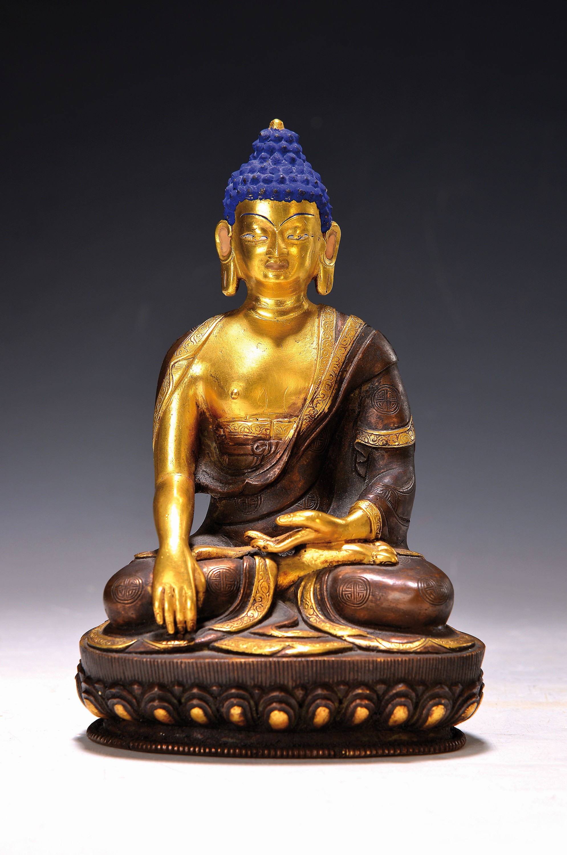 Shakyamuni-Buddha, Nepal, 20. Jh., Bronze, partiell dunkel patiniert, Gesicht und Haare bemalt, verziertes Gewand, Erdberührung, auf Lotussockel, ...
