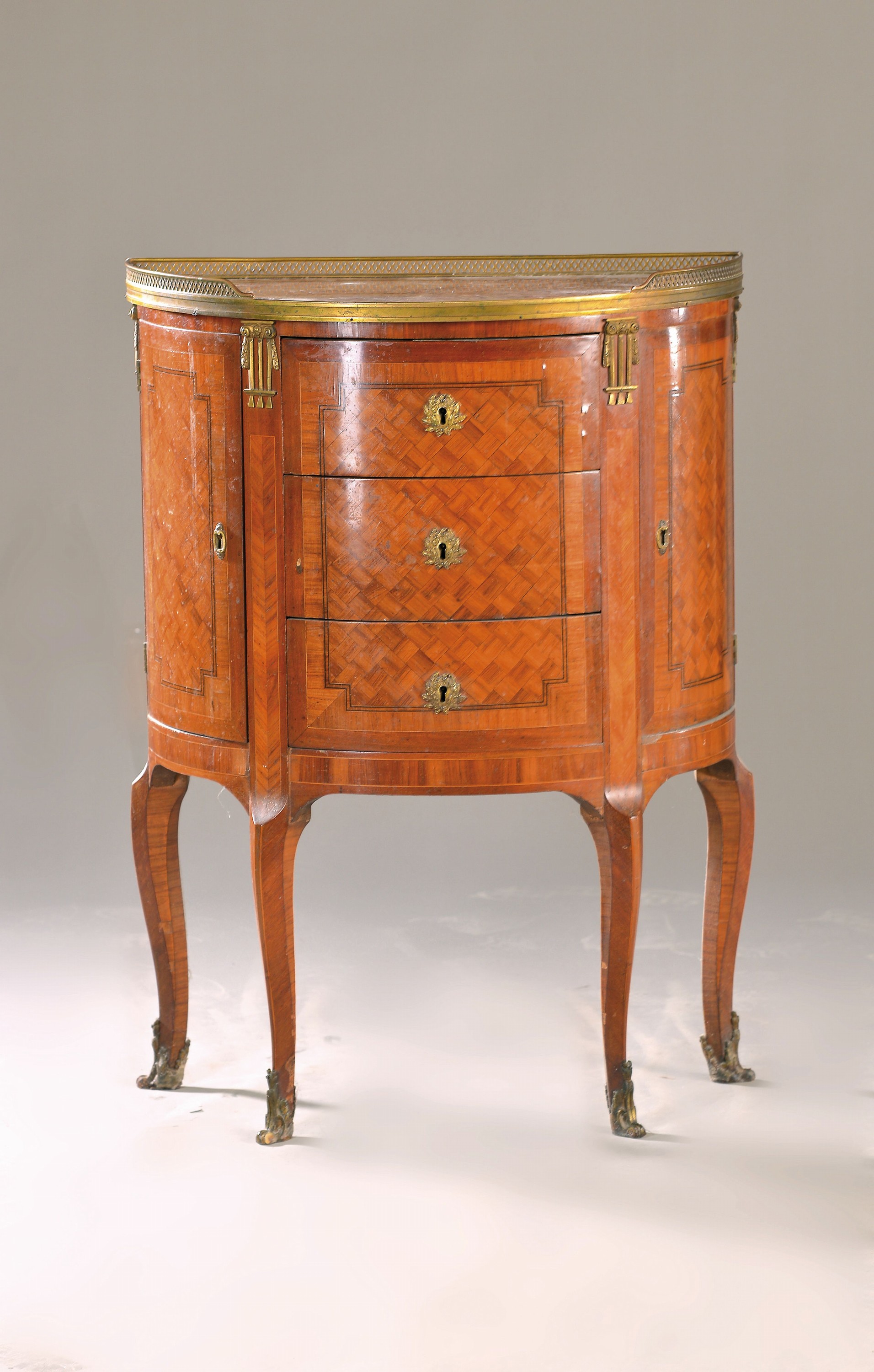 Kleine halbrunde Kommode, wohl Frankreich, um 1900, Mahagonifurnier, z.T. würfelförmig verlegt, 3 Schubladen, seitlich zwei Türen, Marmorplatte, ...