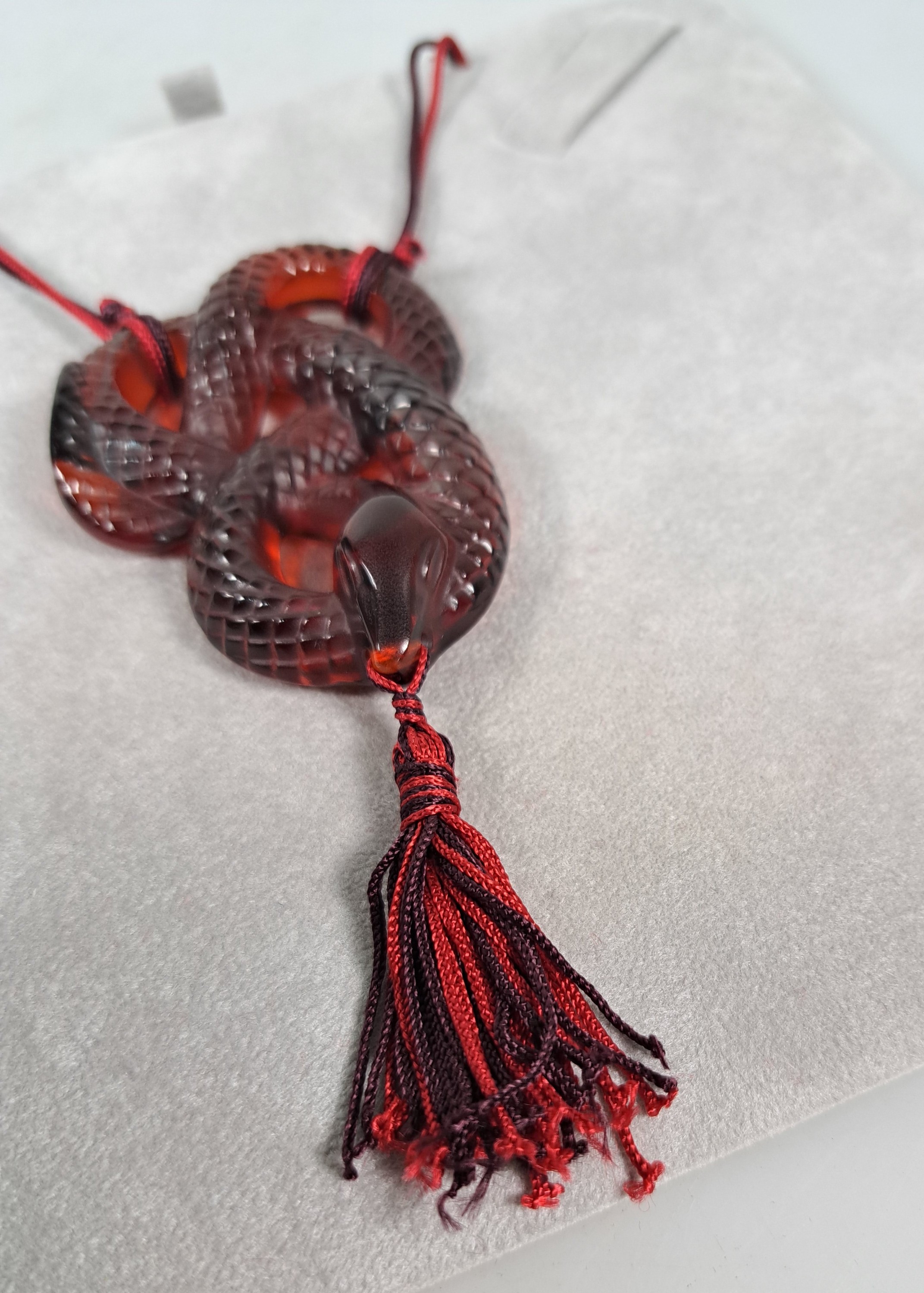 Detail e: Collier Serpent Rouge, Lalique, 20.Jh., rotes Kristallglas in Form einer vielfach gewunden Schlange, z.T. strukturiert, rot- schwarze Seidenquaste im ...