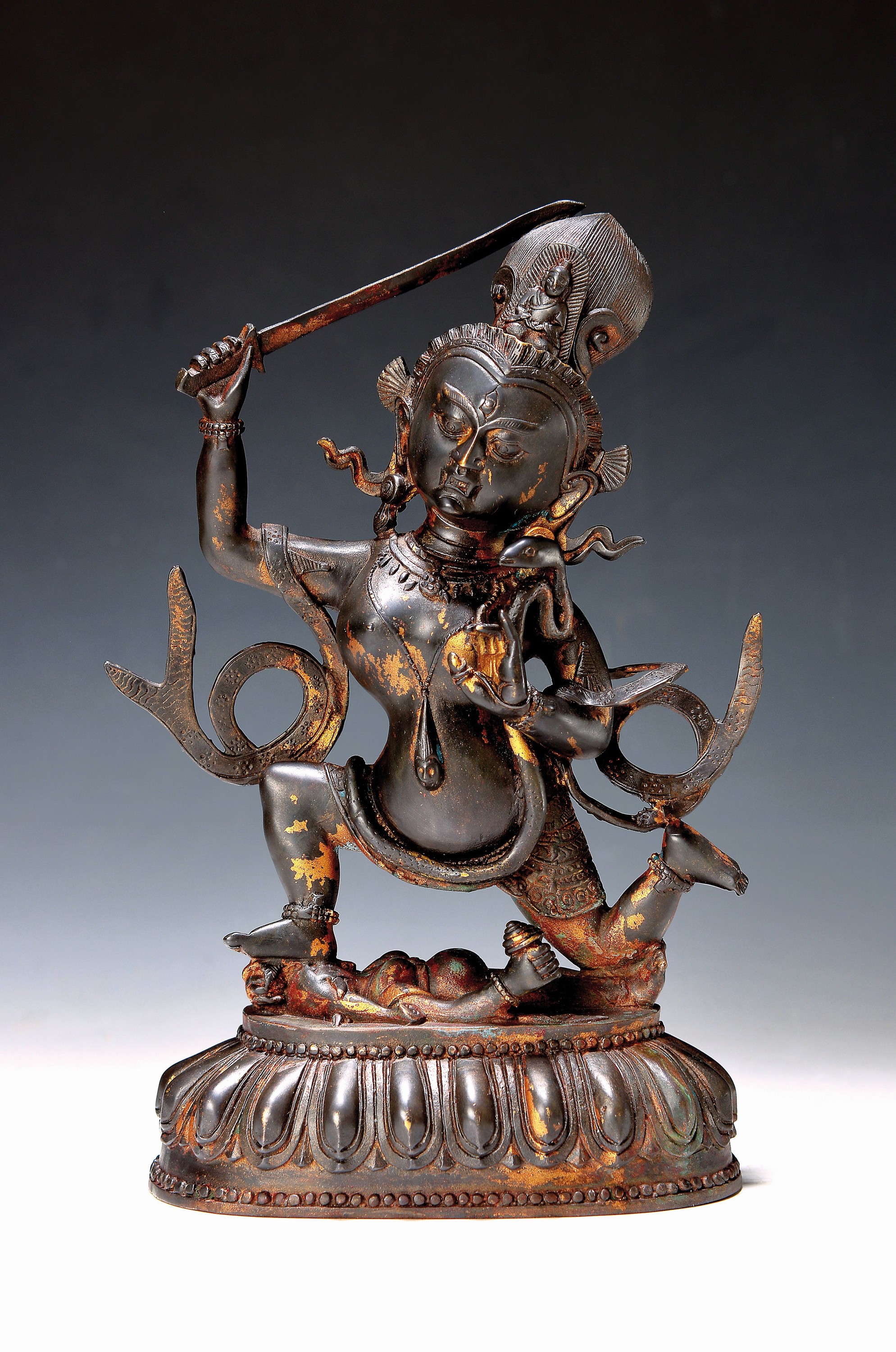 Gottheit Acala, Nepal, 20. Jh., Bronze, zornvolle Gottheit mit Schwert in der rechten hand, unter ihr liegt der Feind am Boden, Acala beißt erzürnt ...