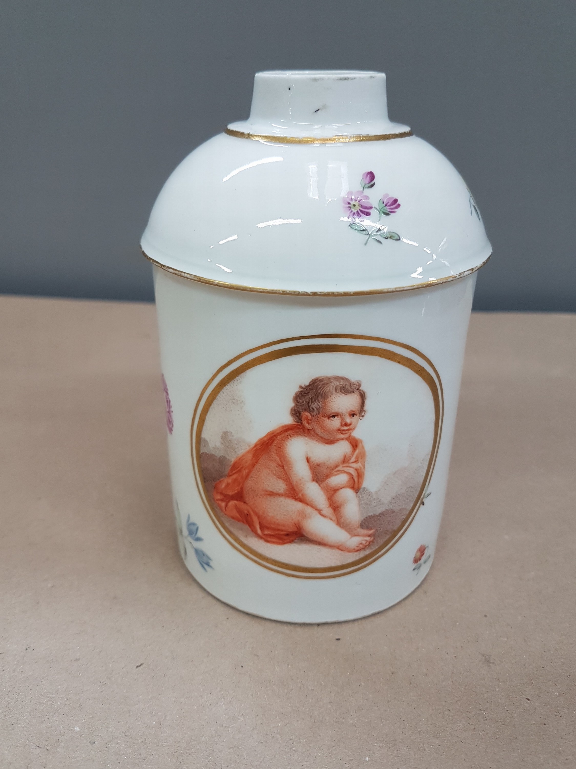 Detail a: Große Teedose Frankenthal, dat. 1779, CT-Marke, Porzellan, im Oval, sitzender Putto mit rotem Mantel, gestreute Blümchen, ohne Deckel, H. ca. 13 cm