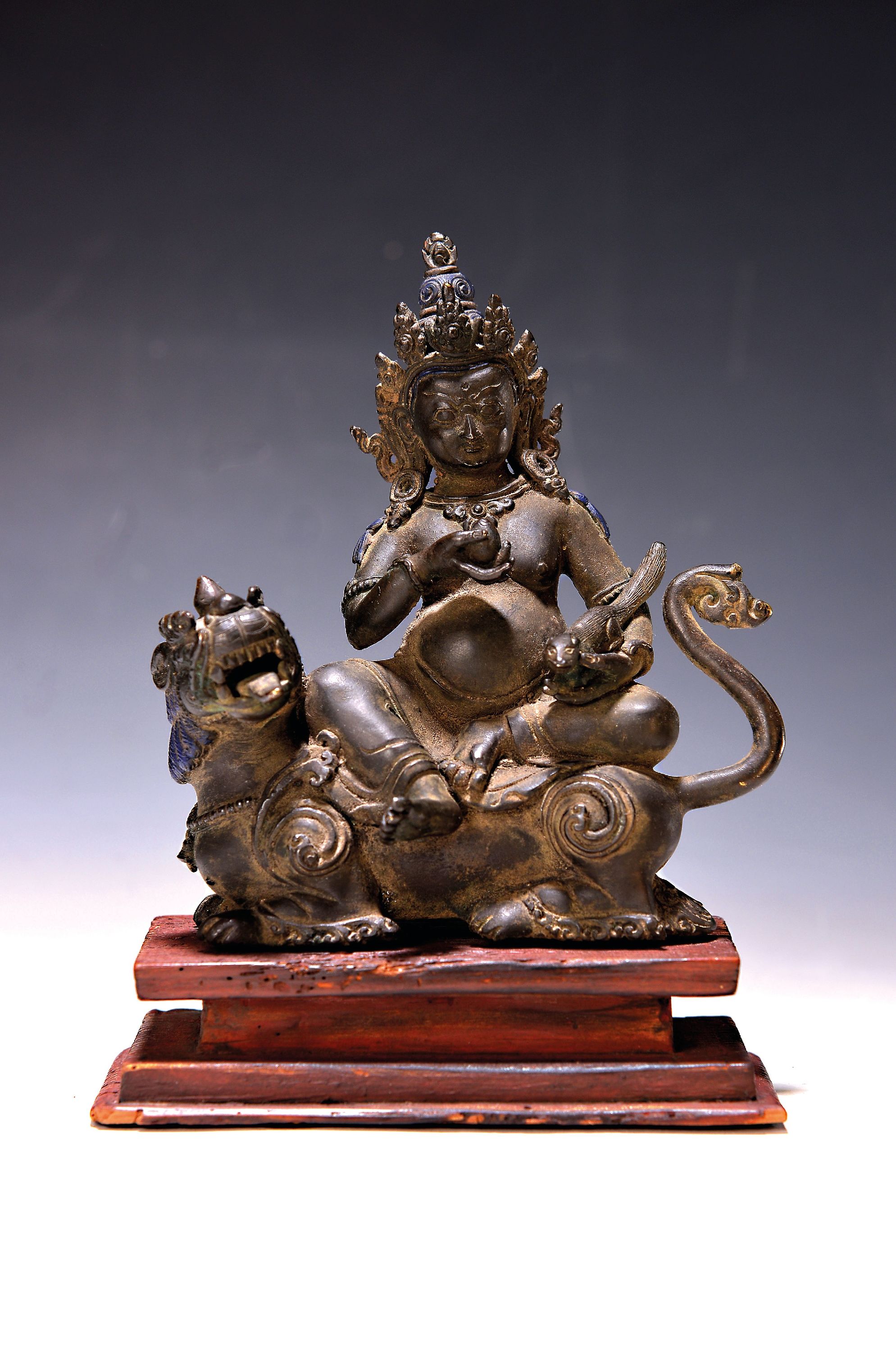 Vaishravana auf Löwe, 20.Jh., Nepal, Kupferlegierung, "Gott des Reichtums", mit einem Mungo in der Hand, auf Holzsockel, H. 19cm