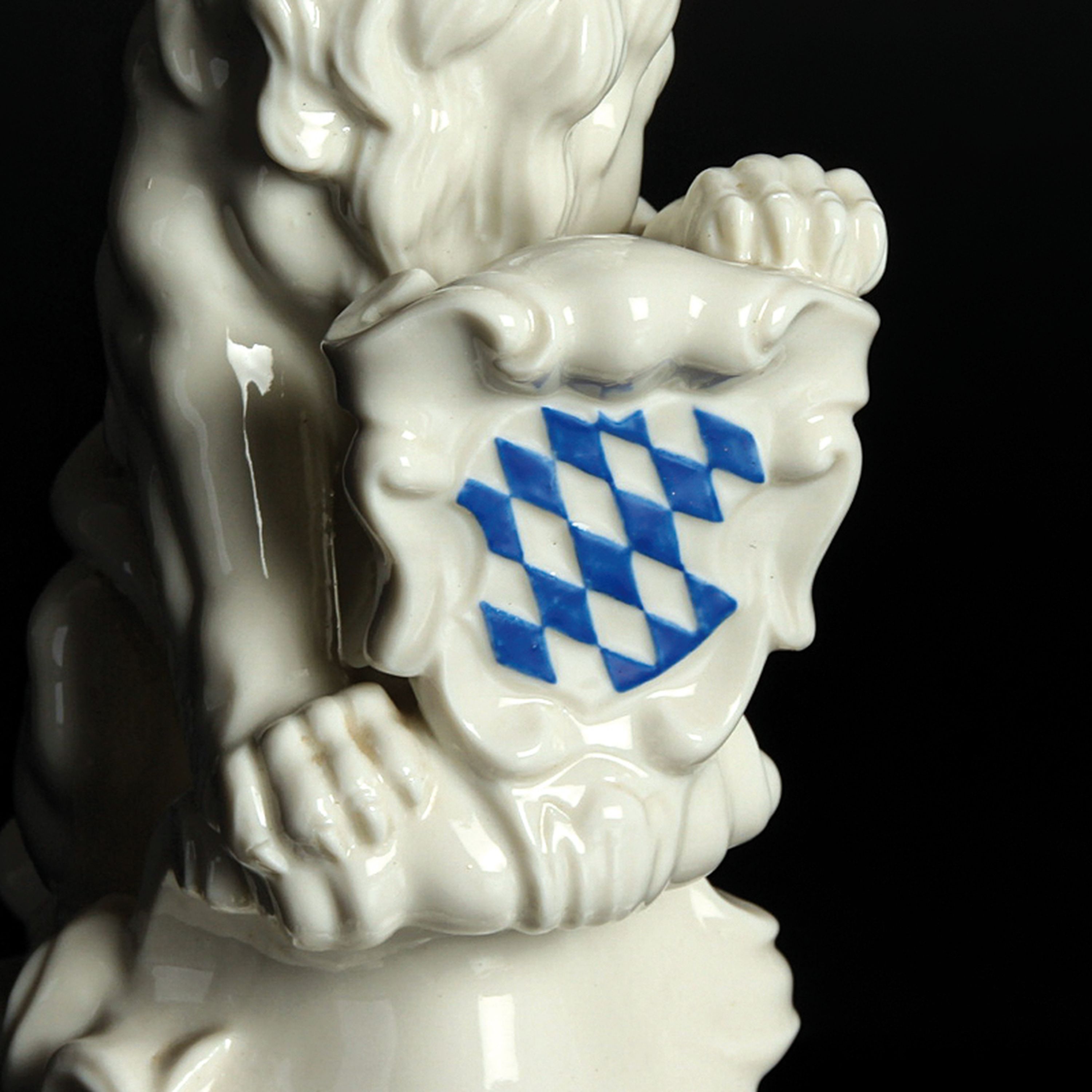 Detail b: Porzellanfigur bayerischer Löwe, Nymphenburg, 20.Jh., Entw. J. Wackerle, Weißporzellan, blau staffiertes Wappenschild, am Boden signiert, H. 23 cm