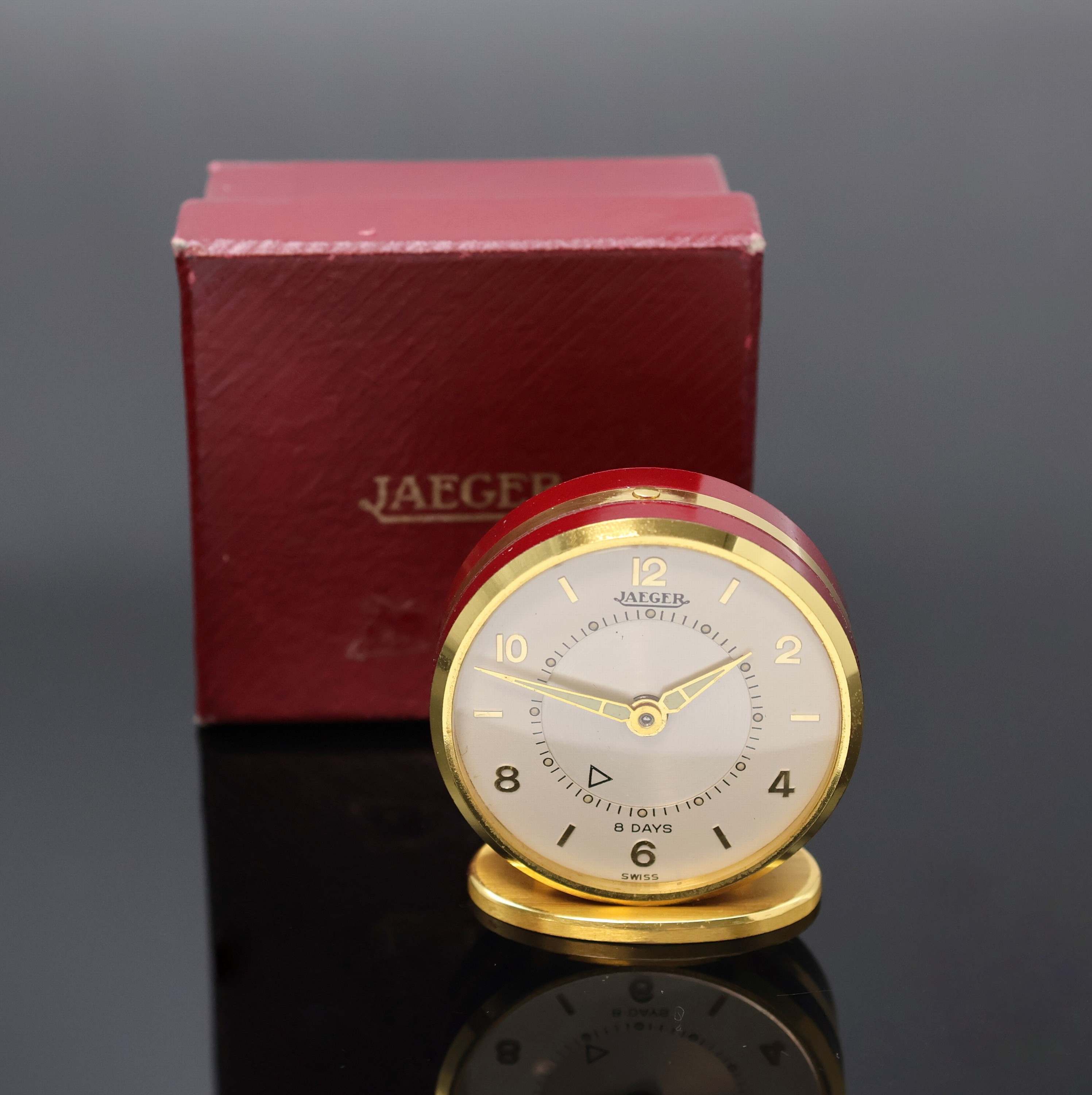 JAEGER kleiner Tischwecker mit 8-Tagewerk, Schweiz um 1960, verg., teils rot lack. Gehäuse, silb. Duoton-Zifferbl. m. aufges. gold. Std.-Ind. u. ...