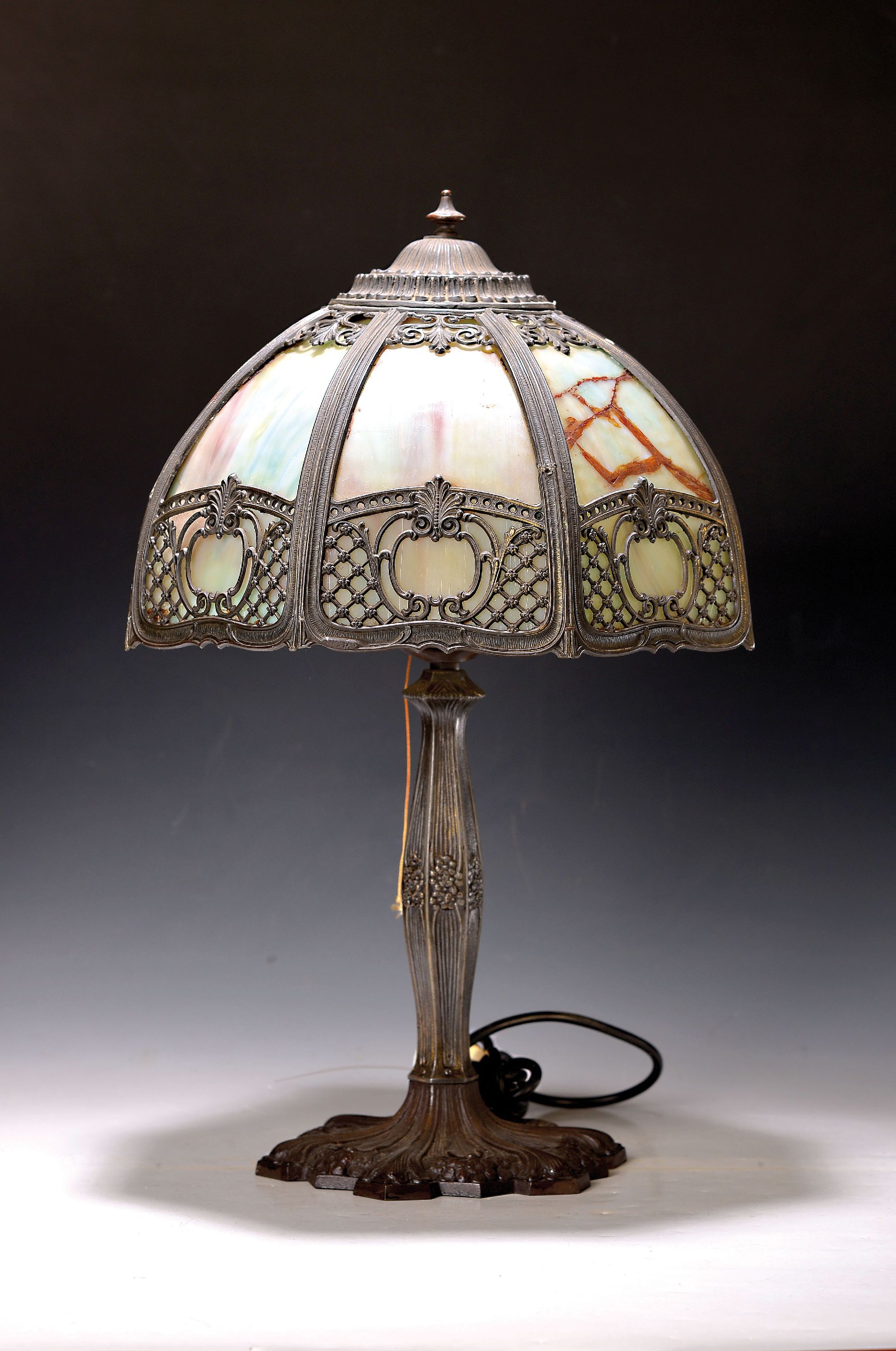 Tischlampe, wohl USA, um 1910/20, Eisenfuß floral verziert, Schirm aus Metall mit leicht farbigen Opakglaseinsätzen, in Durchbruch verziert, zwei ...